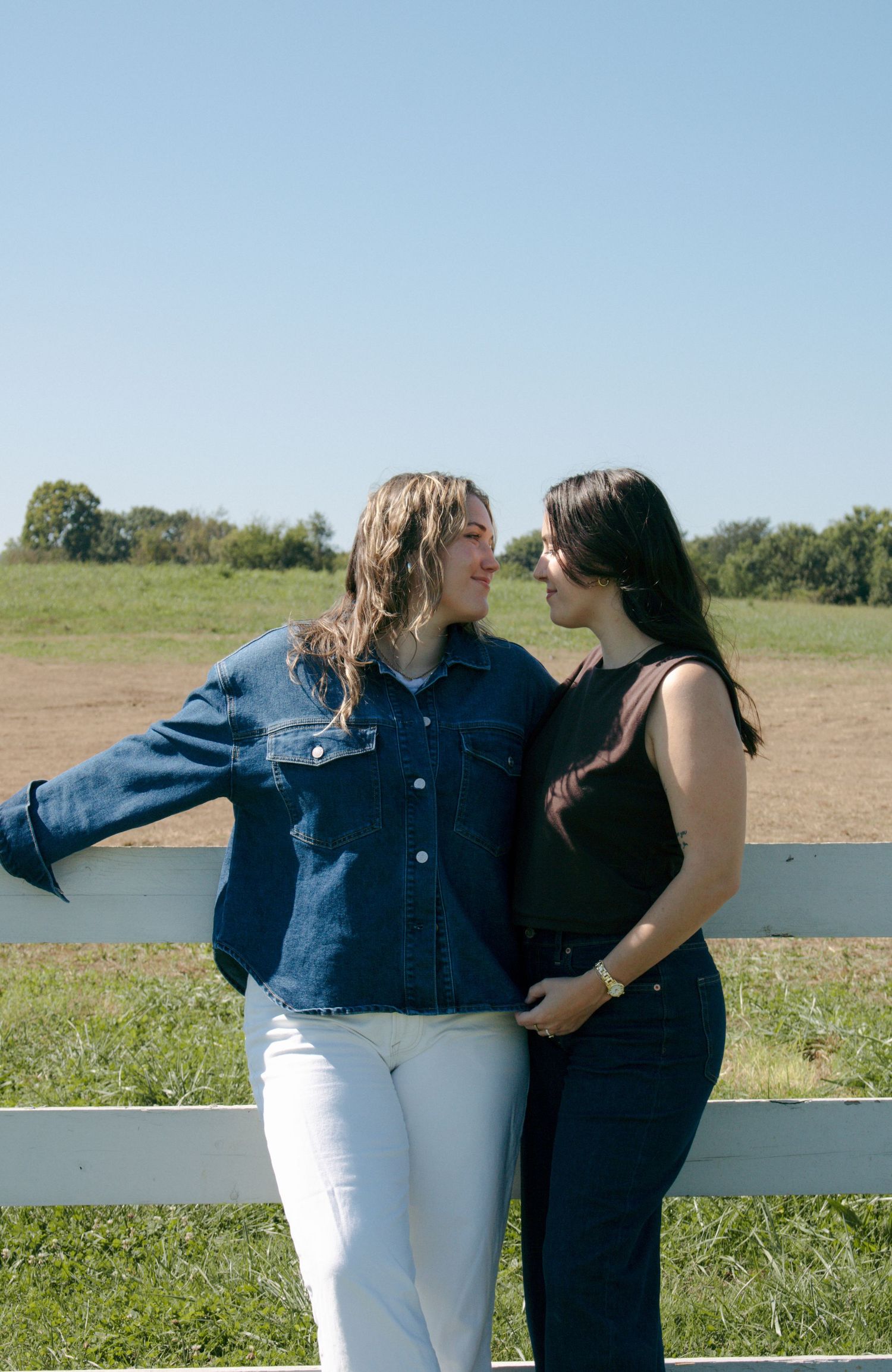 Two people sitting on a white fence share a playful moment outdoors.