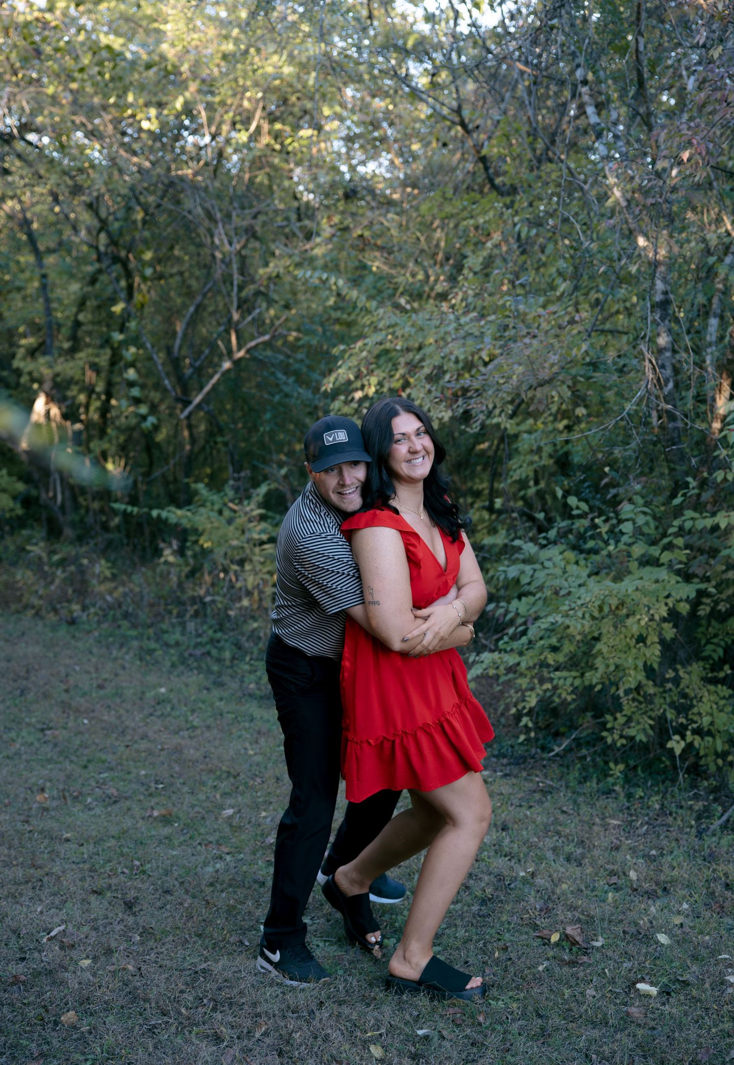 A couple shares an intimate moment outdoors surrounded by autumn trees during a photoshoot.