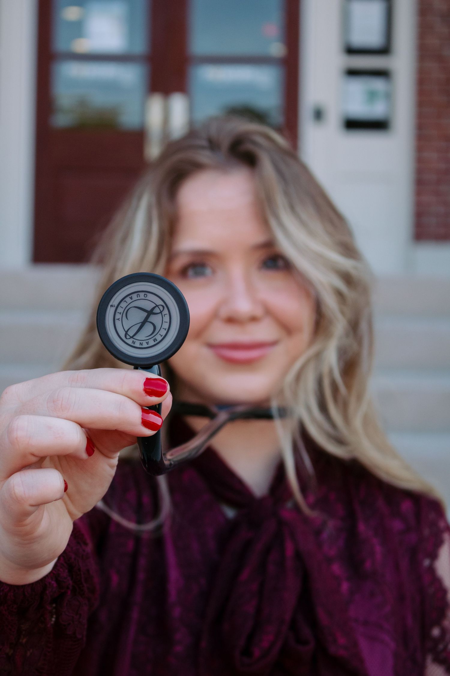 Person in purple sweater holds up black lens cap against blurred background.