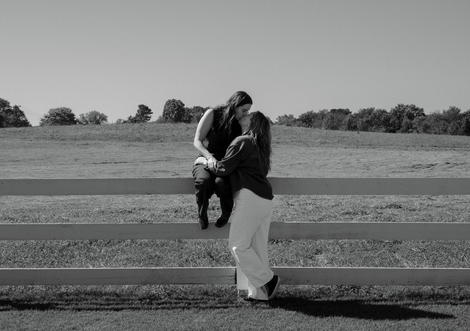 A black and white photo of people sitting on a fence in silhouette.