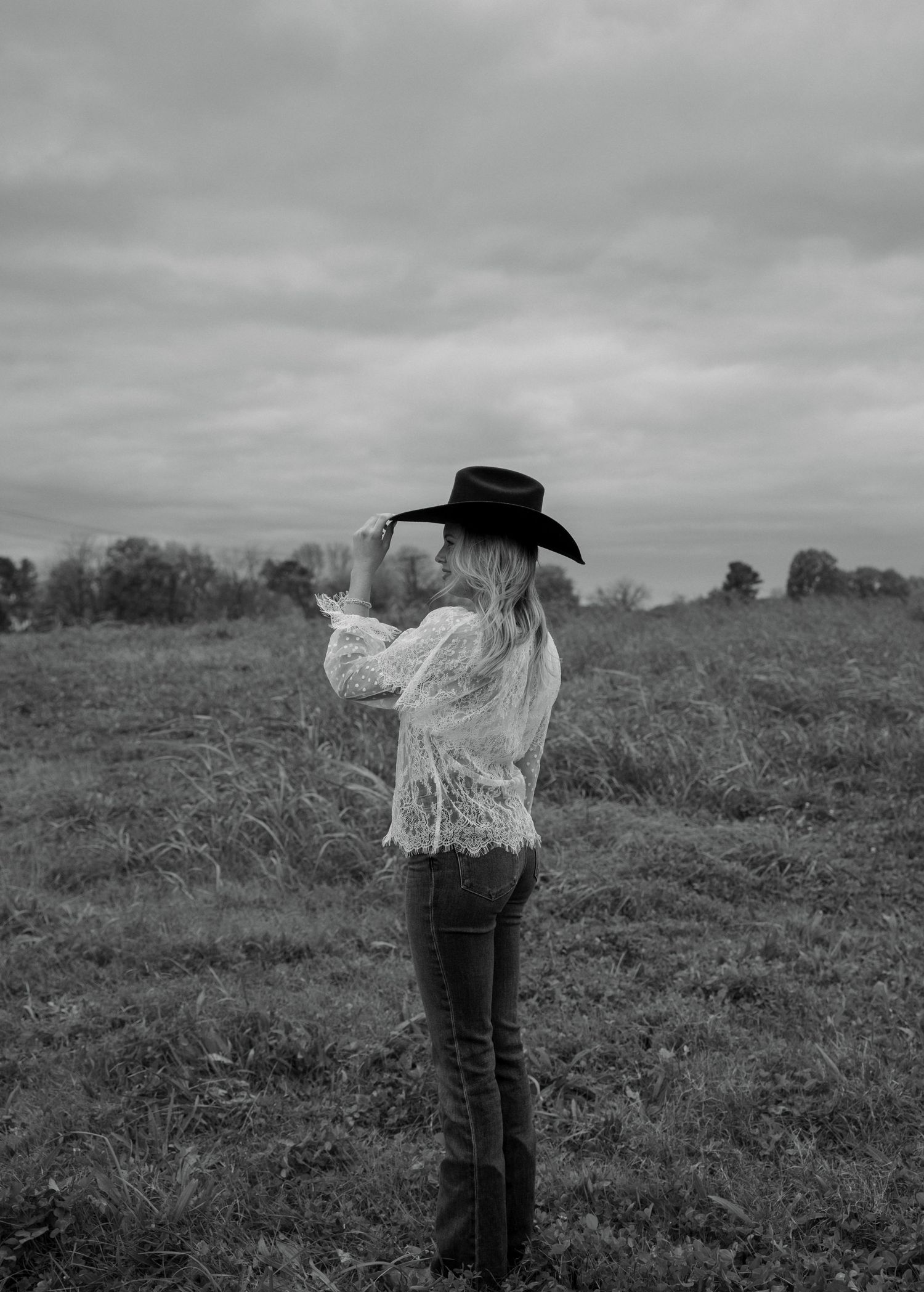 A figure in a flowing white dress stands against a cloudy sky in a dramatic black and white landscape composition.