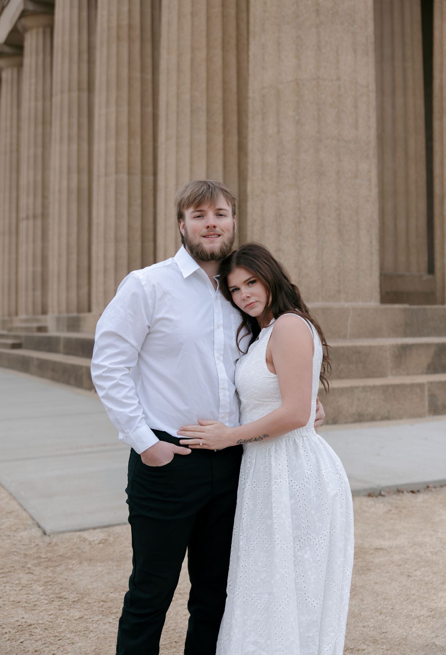 A couple in formal attire shares a romantic moment in front of a columned building.