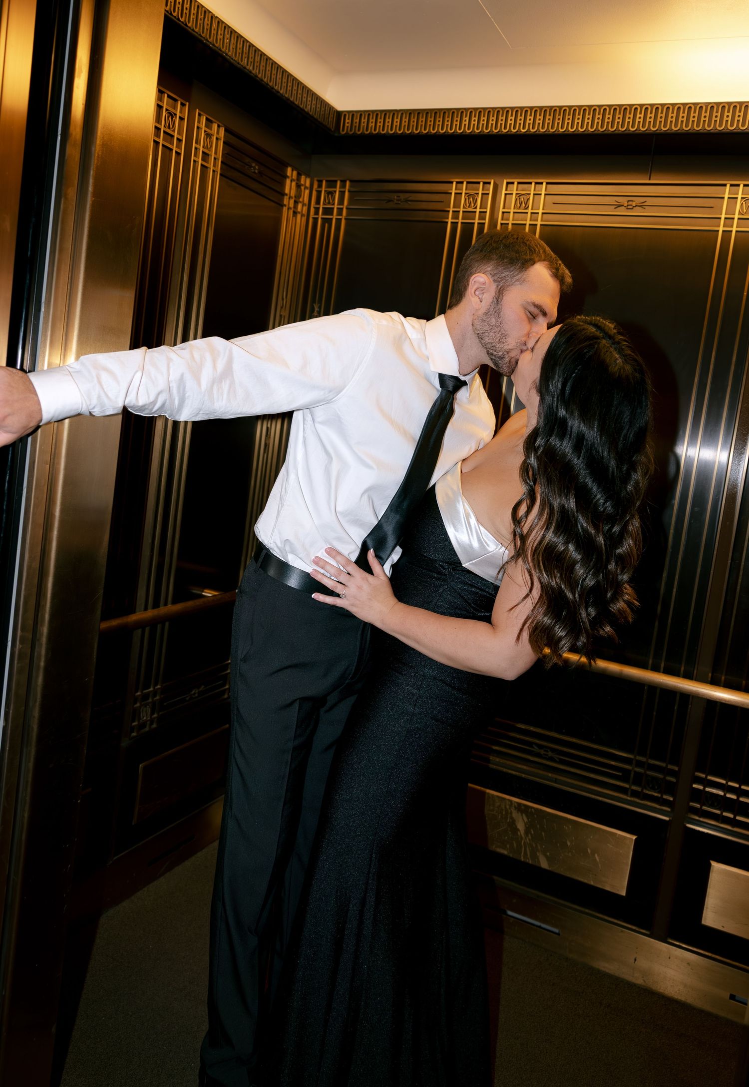 A couple in formal attire performs a dramatic dance dip pose in an elegant hallway with gold trim decor.