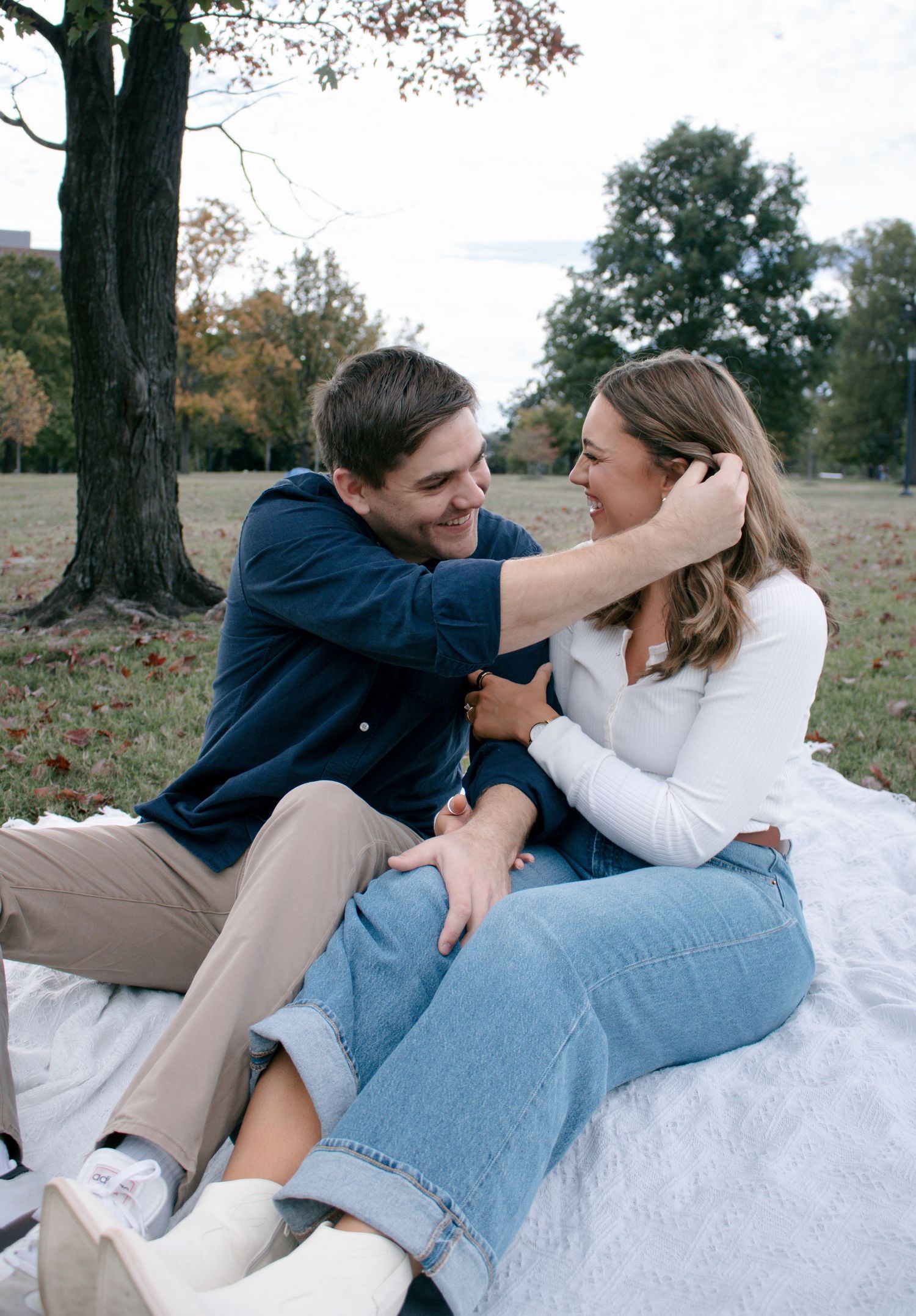 A couple in casual attire shares tender moments while relaxing on a white blanket outdoors during autumn.
