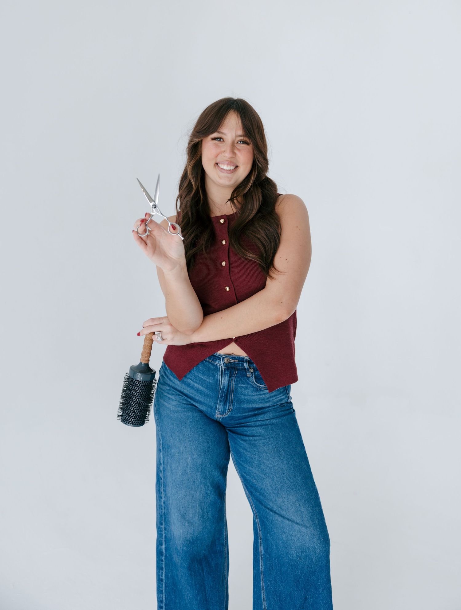 Person wearing a burgundy sleeveless top and wide-leg blue jeans poses playfully against a white background.