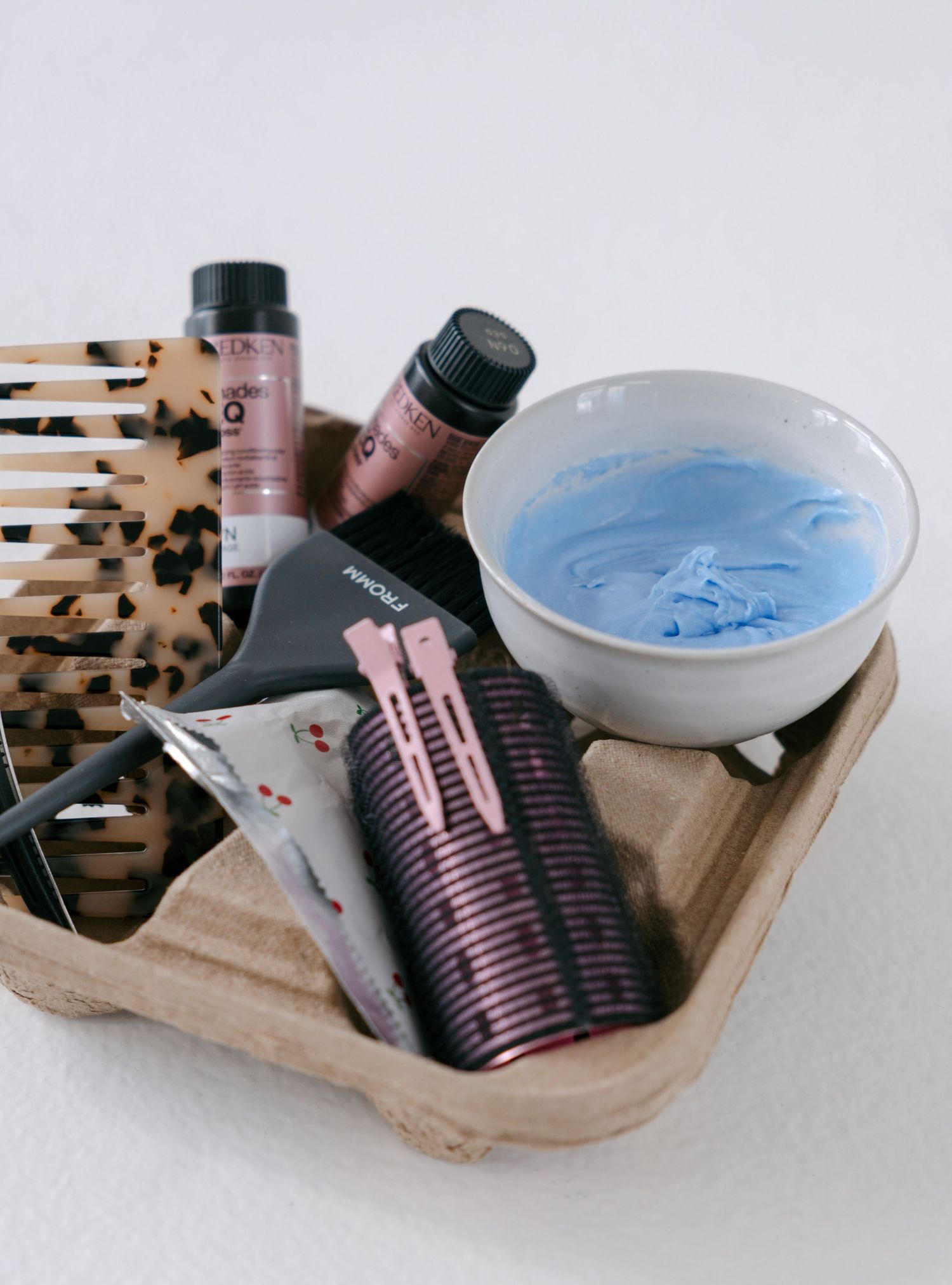 Wooden tray with hair dye tools including a tortoise shell brush, blue color bowl, sectioning clips, and Redken hair color bottles.