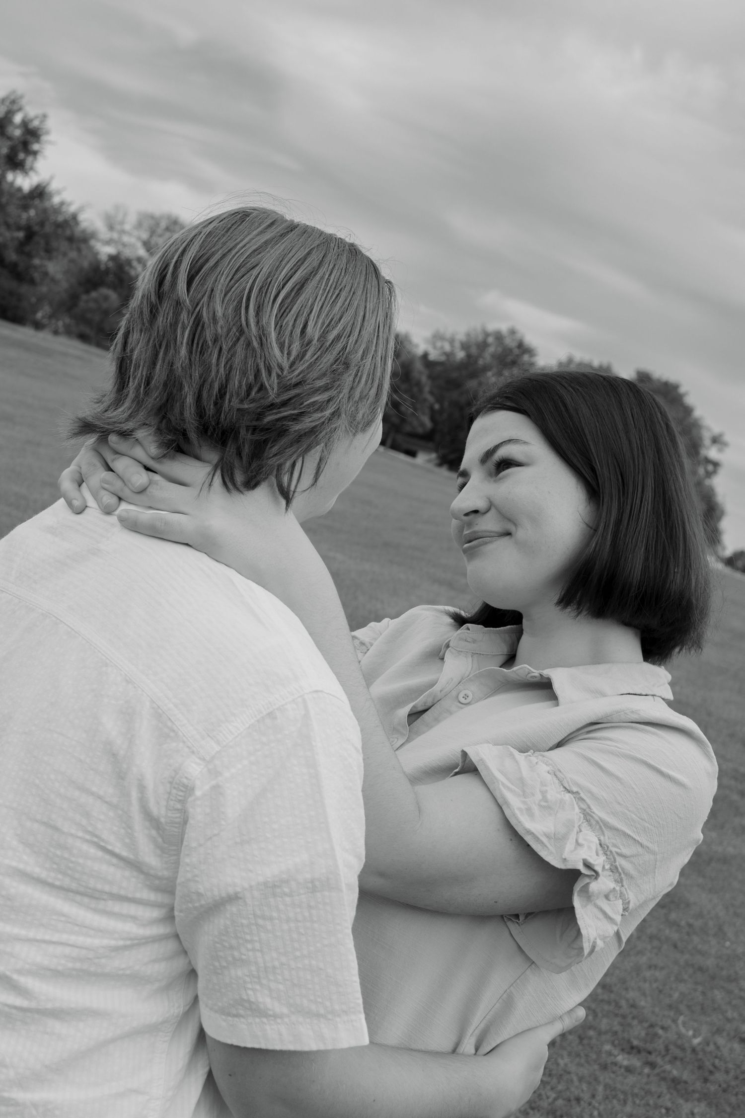 An intimate black and white photo of a couple sharing a tender moment outdoors.