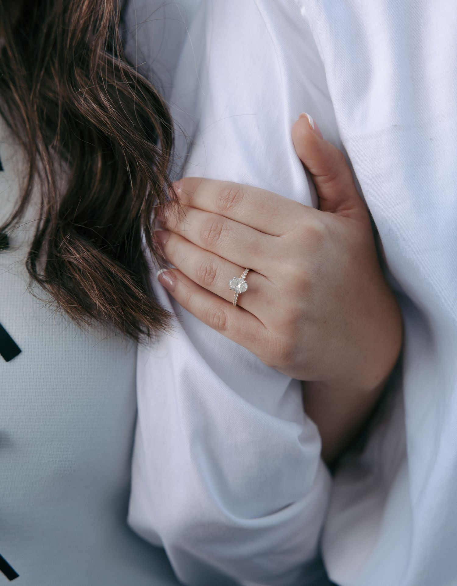 Close-up view of an engagement ring on a hand wearing a white sweater, showing the sparkle of the diamond solitaire.