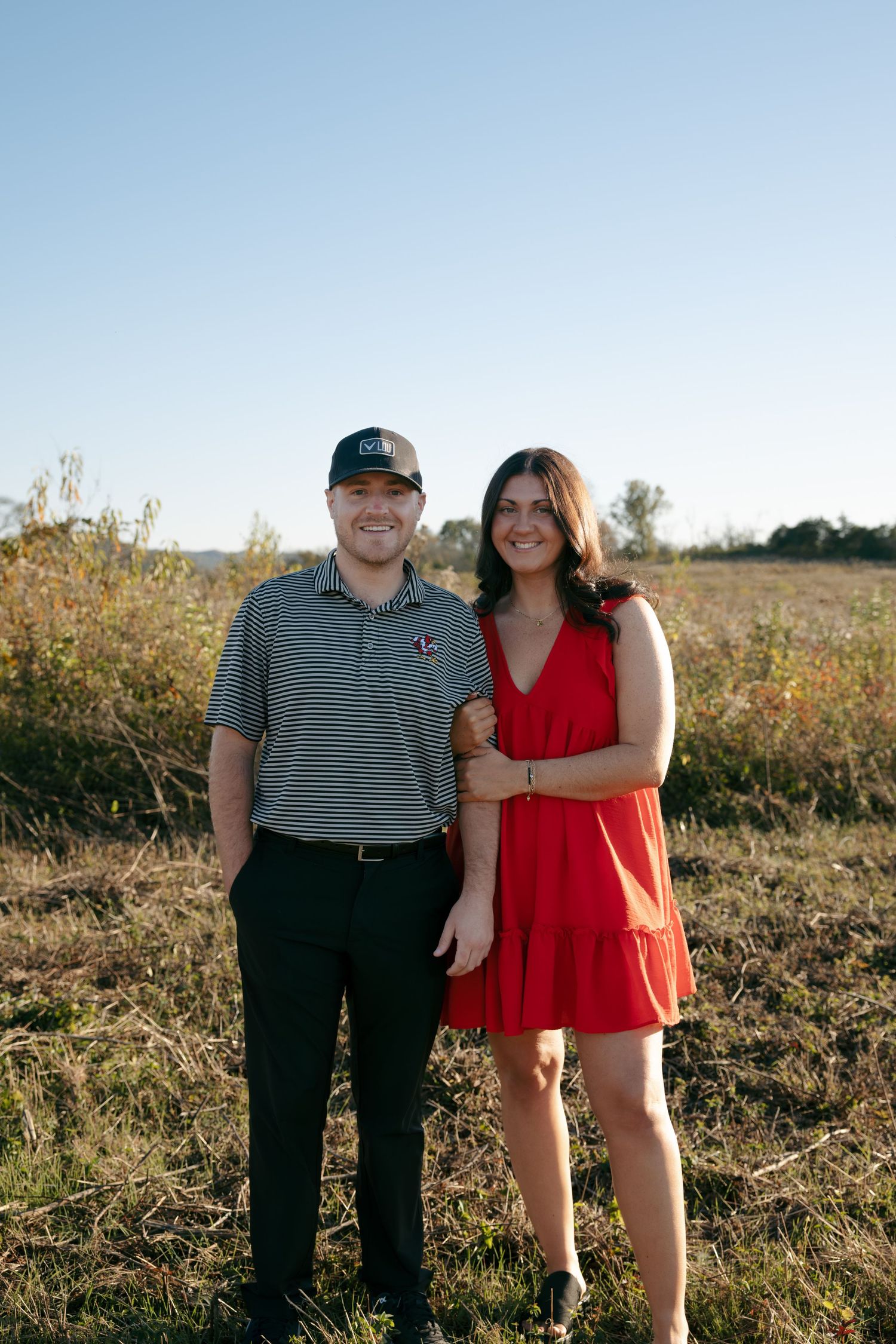 A couple poses together in a sunny outdoor field during golden hour.