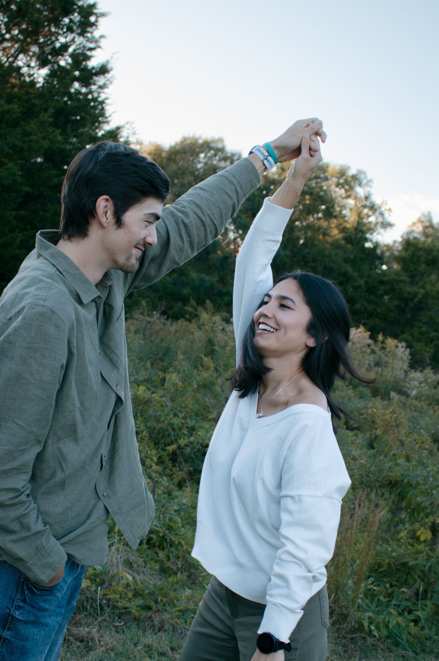 A playful couple dancing together outdoors with natural scenery in the background.
