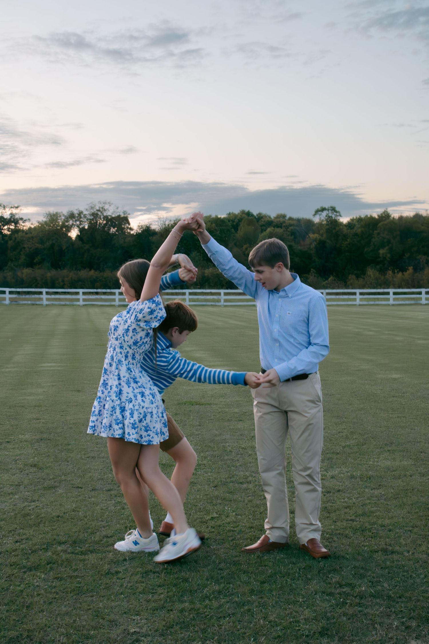 A couple dancing and twirling together in a grassy field at sunset.