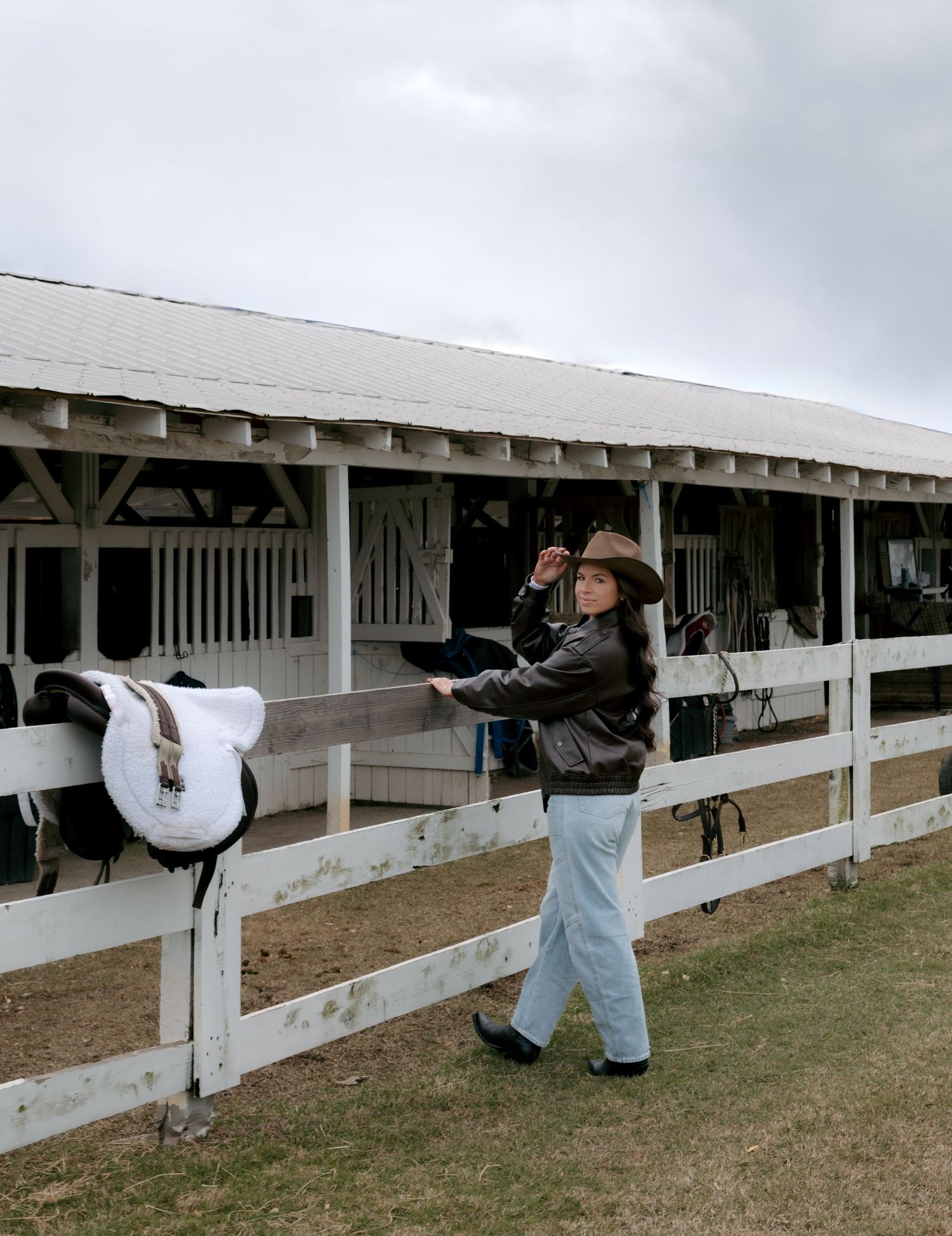 People in protective suits spraying disinfectant on white wooden fence posts at a farm or ranch facility.