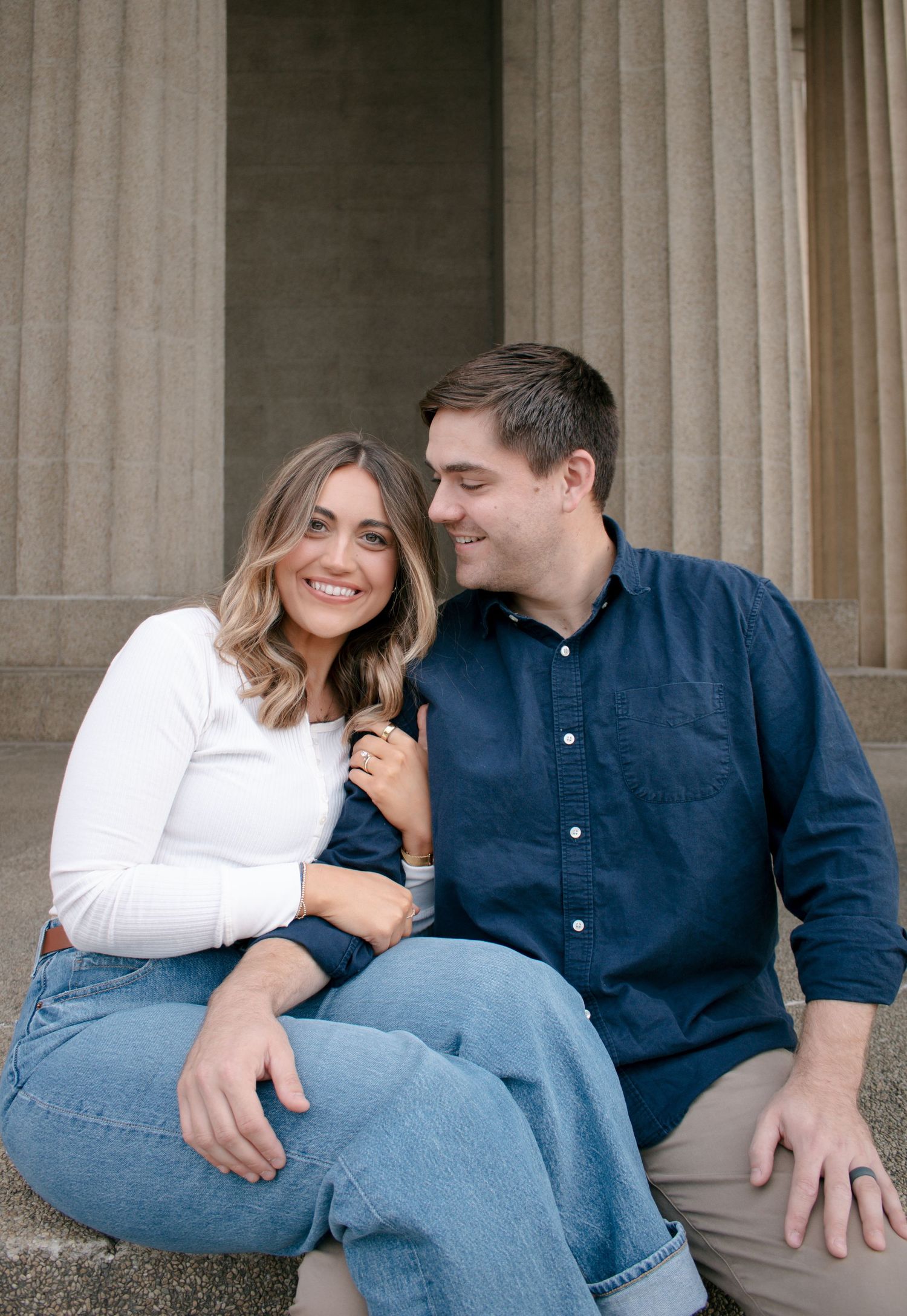 A couple in matching blue jeans and casual attire share intimate moments while sitting on stone steps.