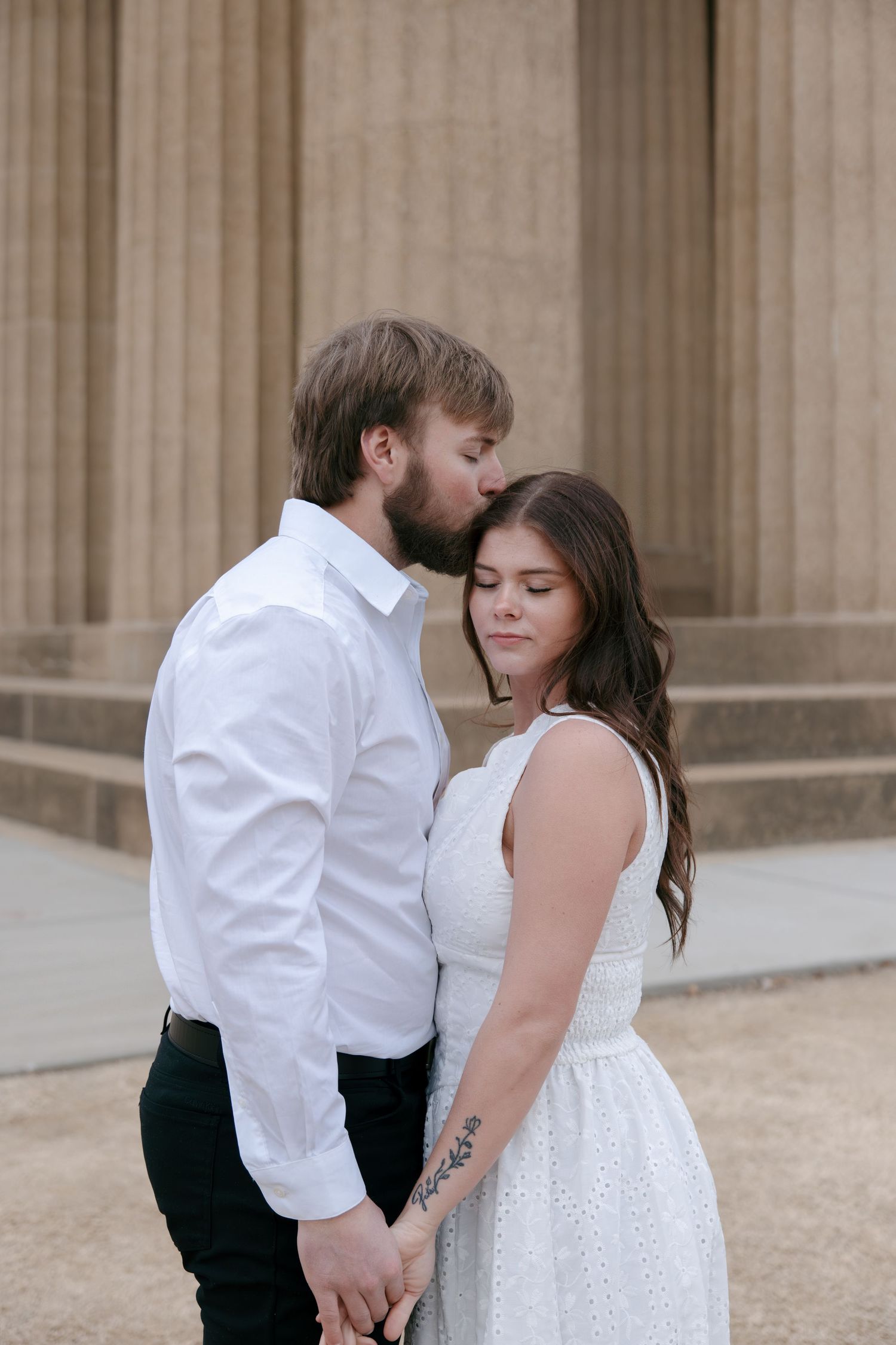 Romantic couple in formal attire share an intimate moment on stone steps of a classical building.