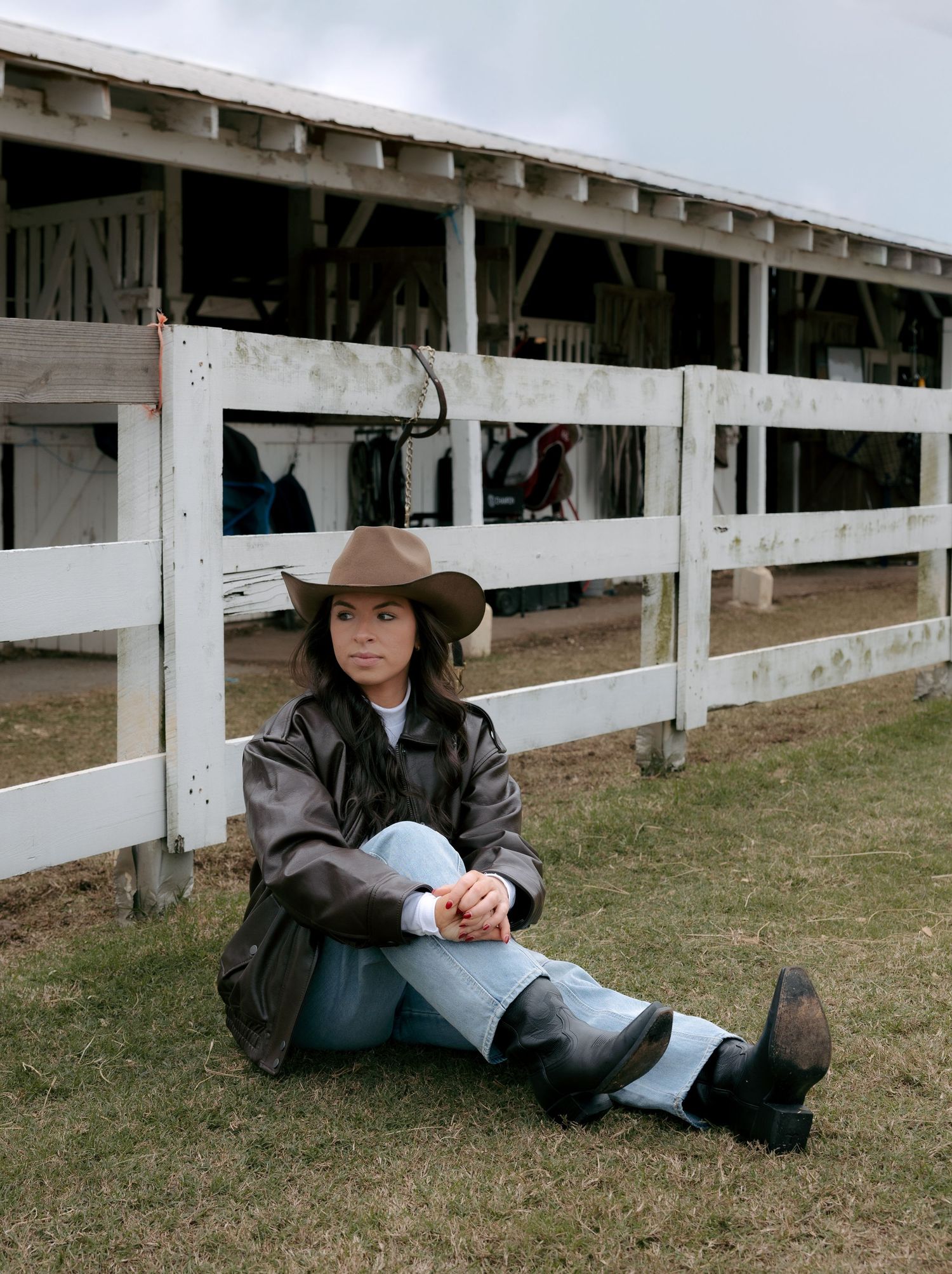 A figure in western attire sits on grass beside a white fence in a series of contemplative poses.