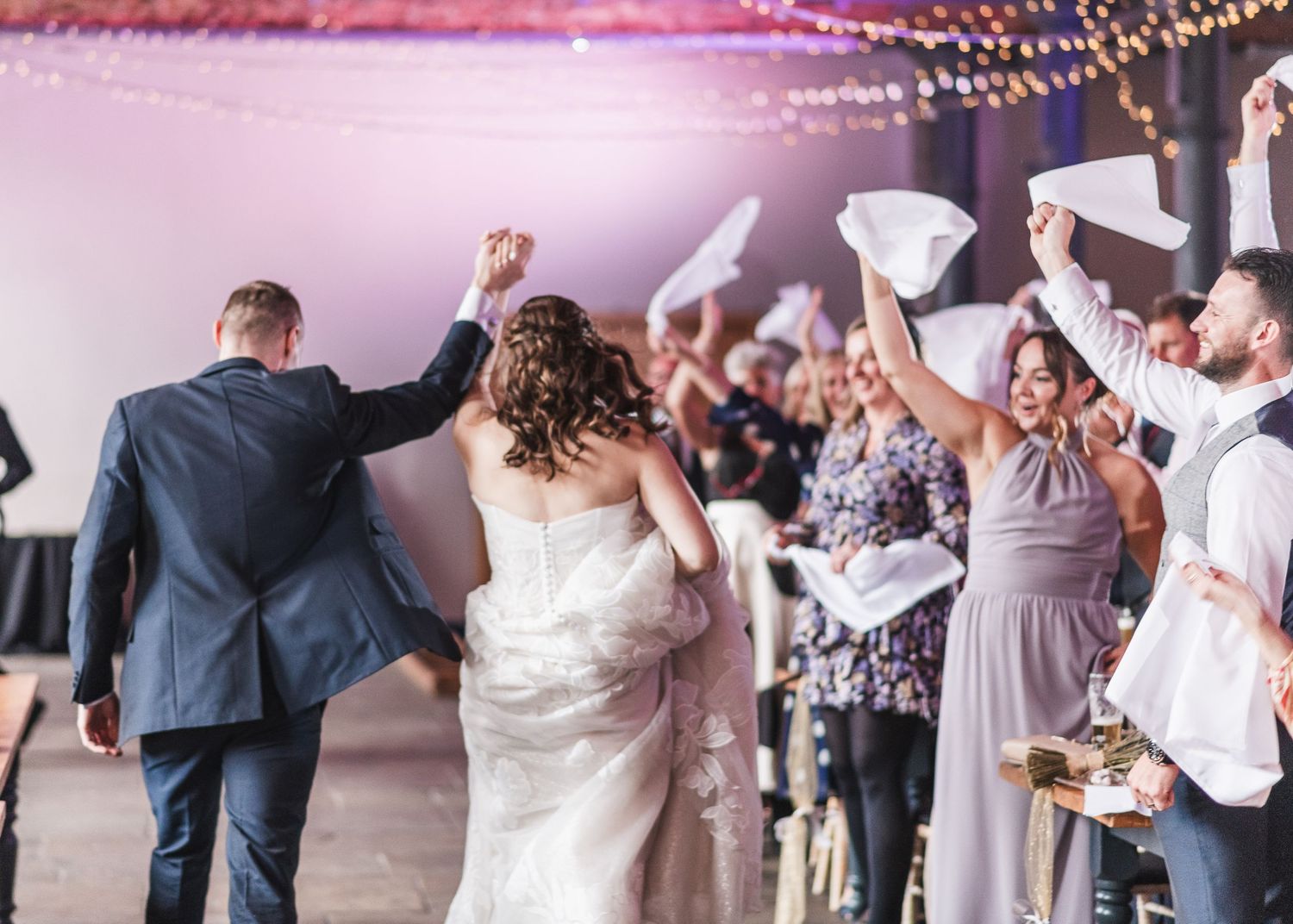 Wedding celebration with string lights and guests dancing on a pink-lit dance floor. Ephemera.