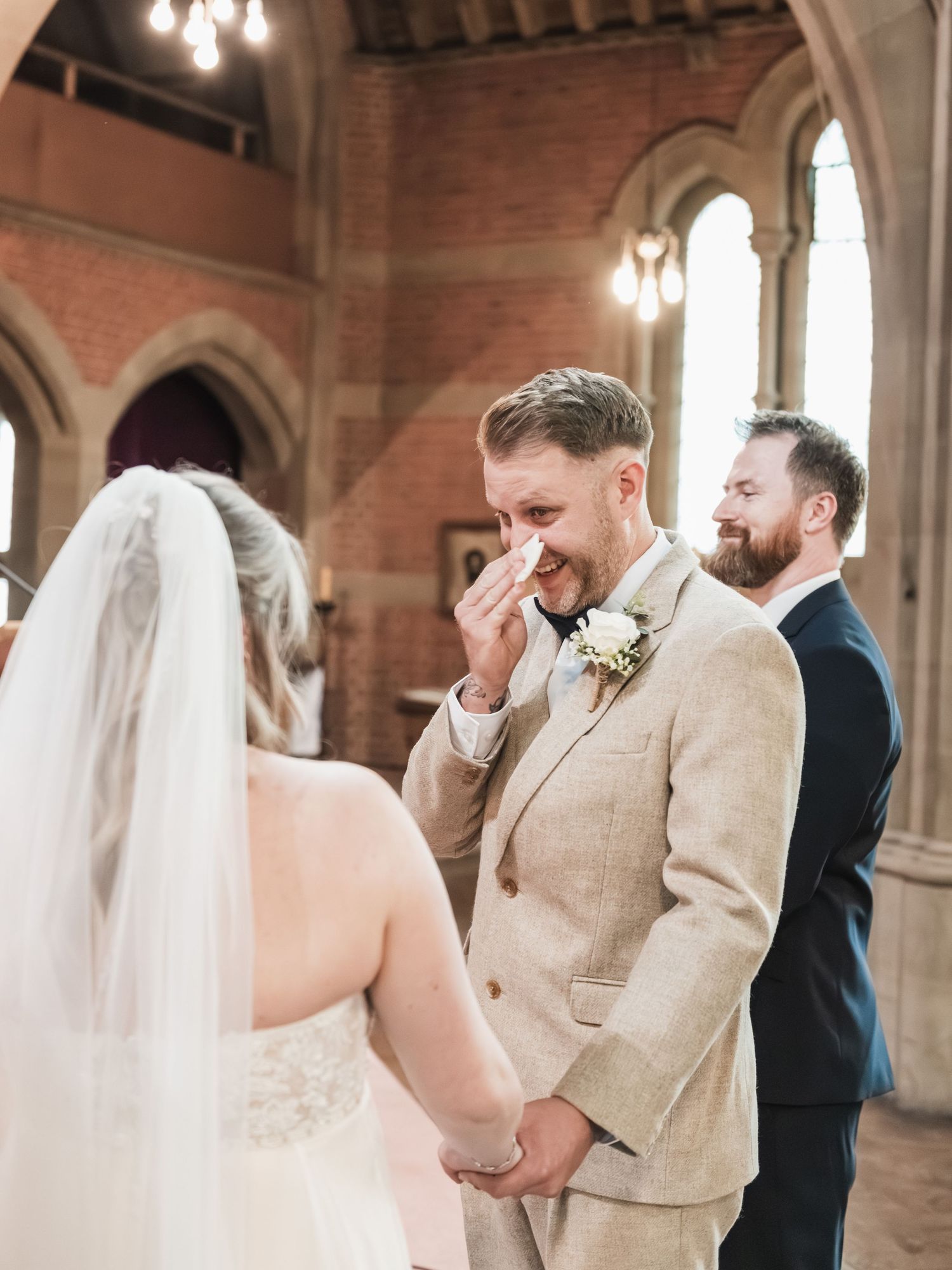 Emotional first look moment between wedding couple in an elegant church setting with arched ceilings and chandeliers.