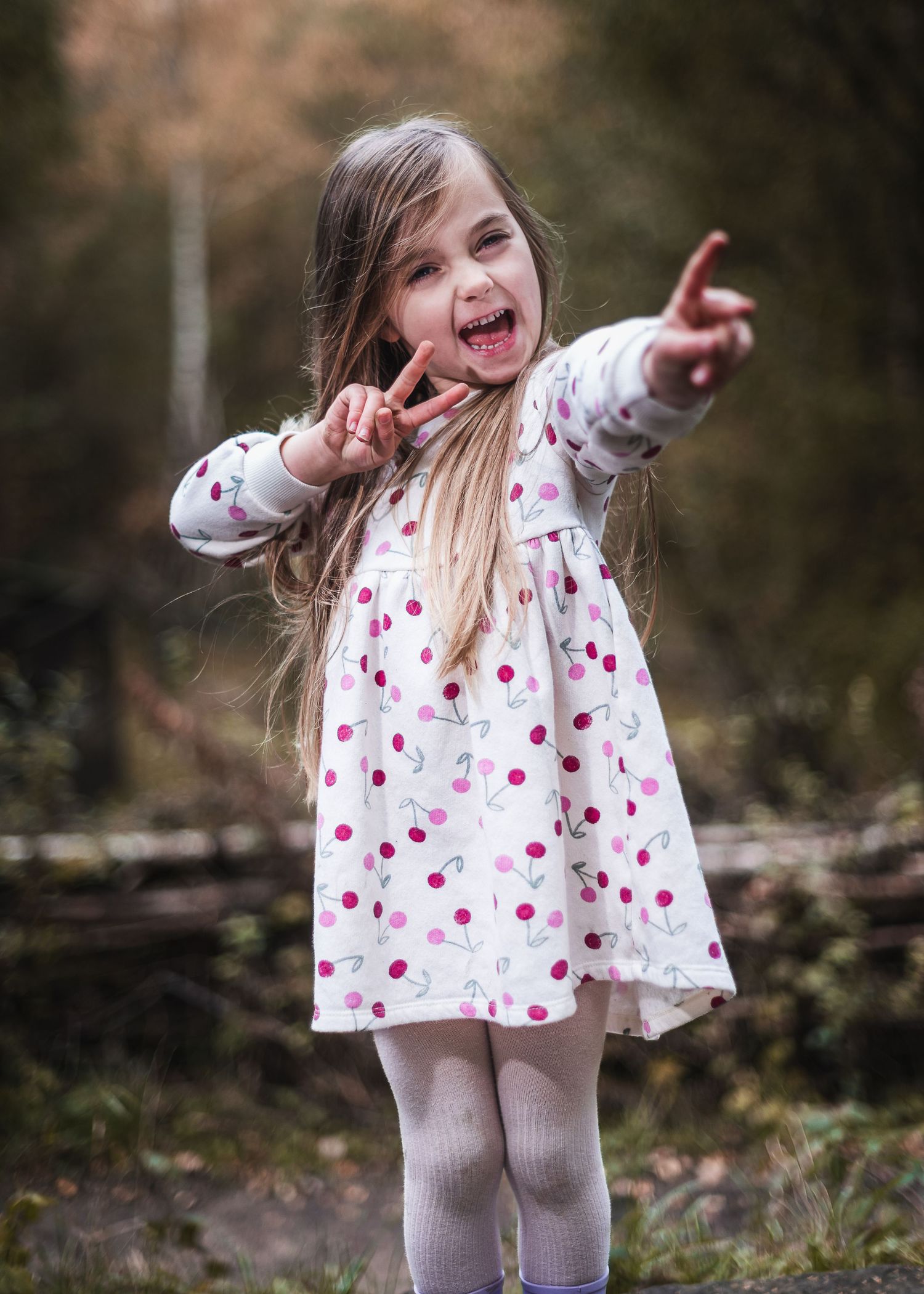 A joyful child in a polka dot dress points and gestures expressively while playing outdoors. Ephemera.