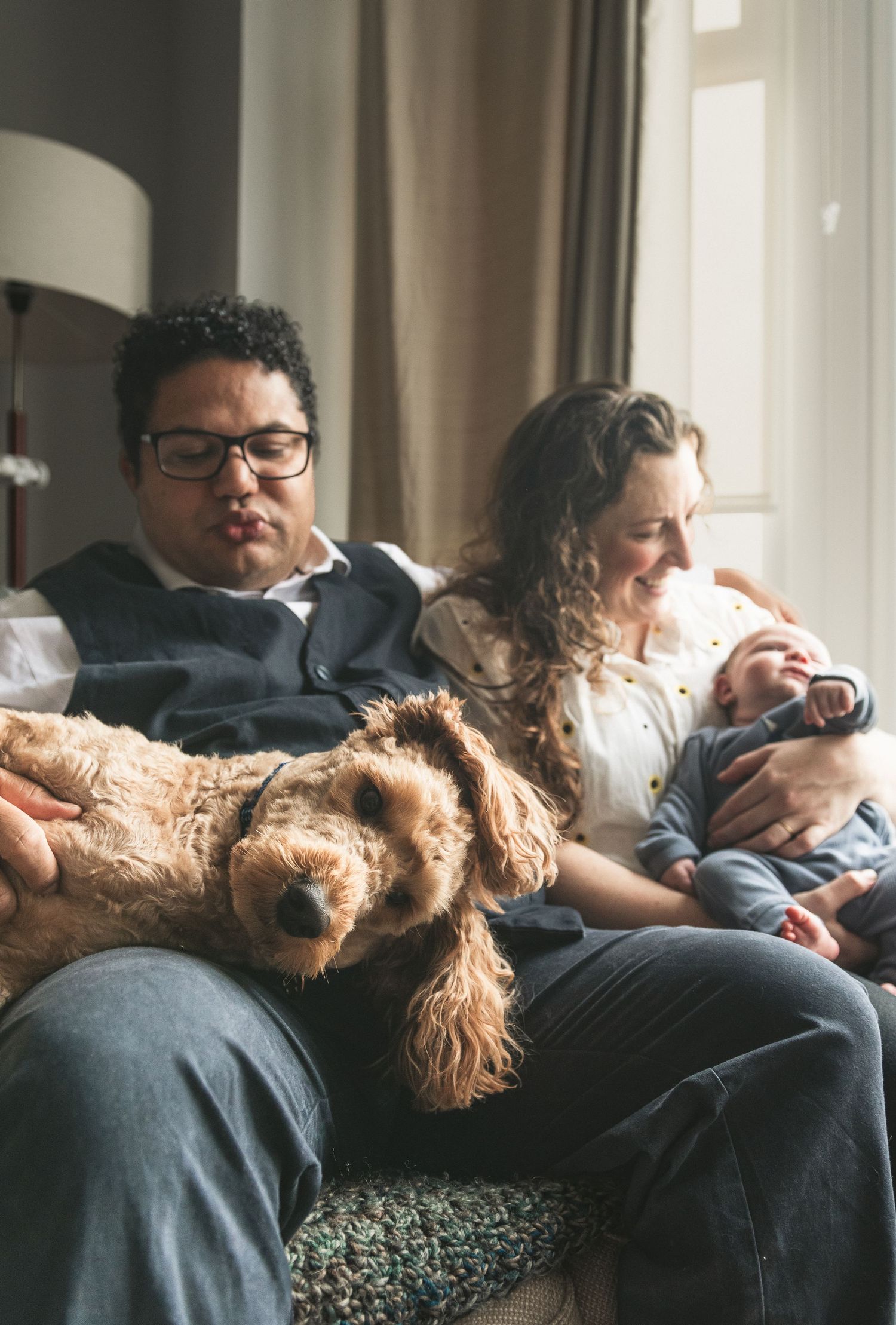Family relaxing on couch with sleeping dog and newborn baby in casual home setting. Ephemera.