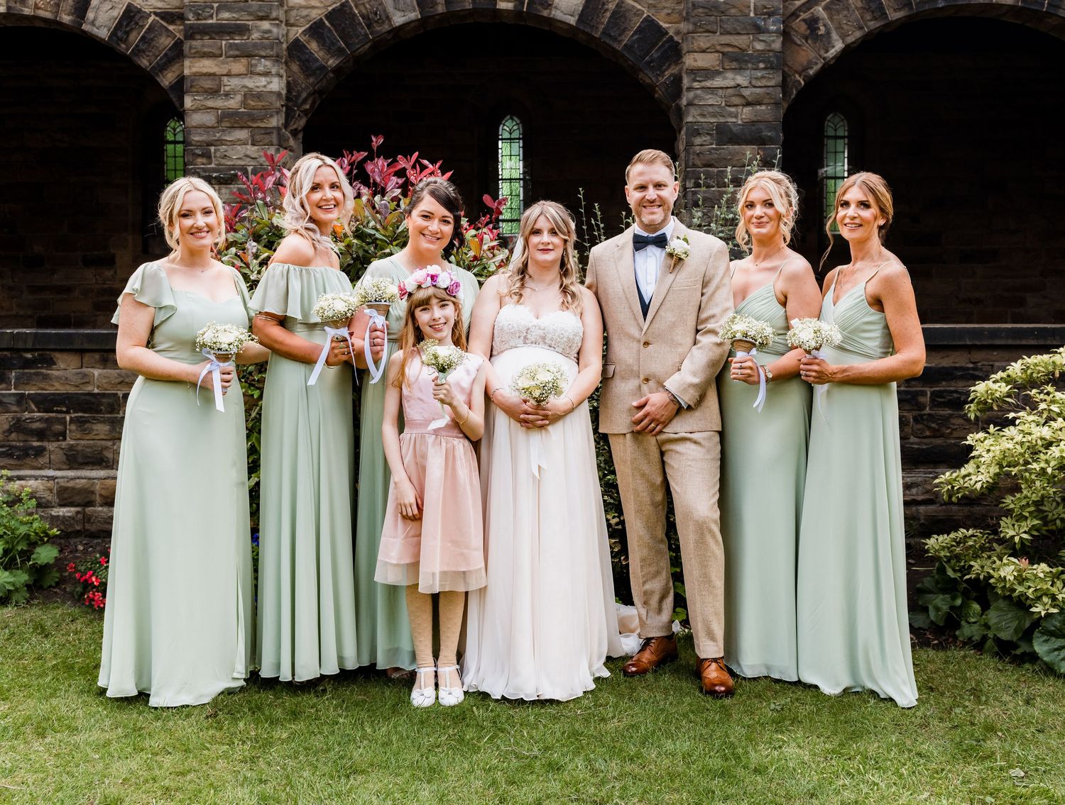Wedding party in mint green dresses and tan suits posing together on church grounds. Ephemera.
