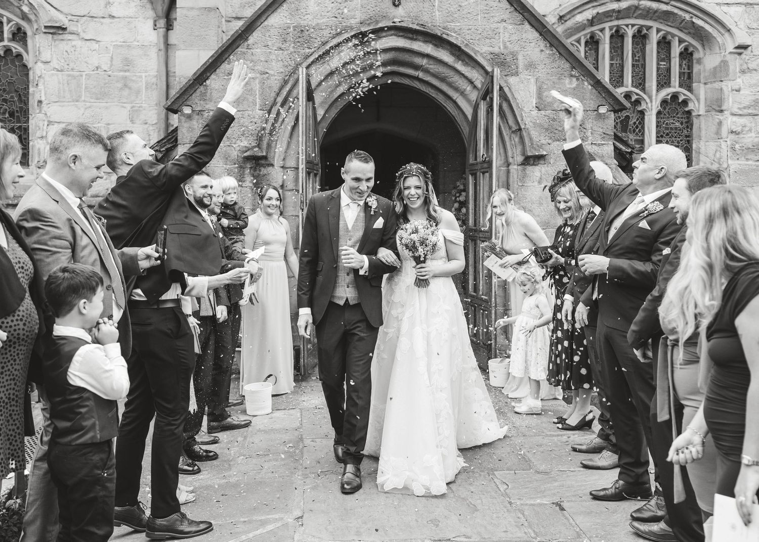 Wedding party lined up outside a historic stone church with gothic architecture. Ephemera.