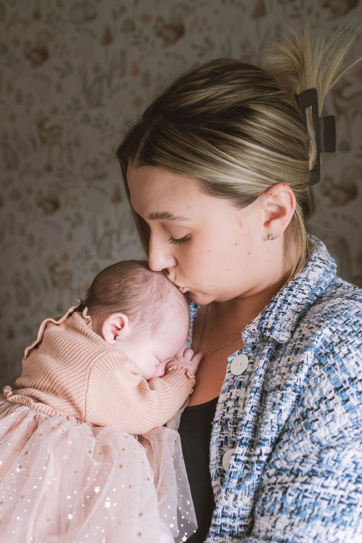 Tender moment between mother and baby in pink dress against stone wall background. Ephemera.