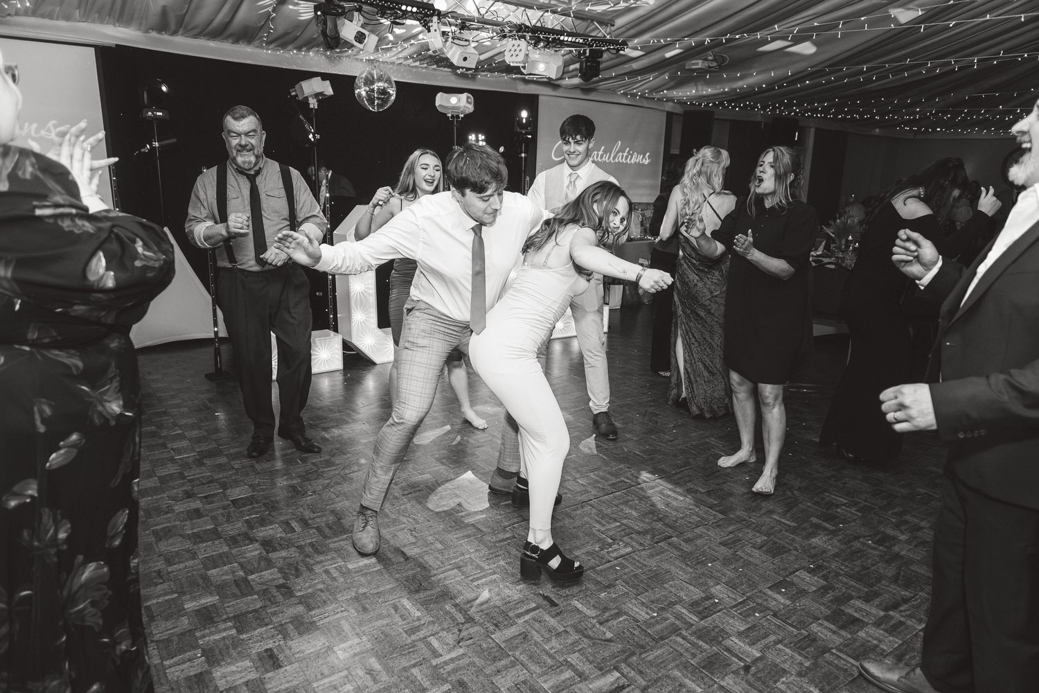 Black and white photo of wedding guests dancing energetically on parquet floor. Ephemera.
