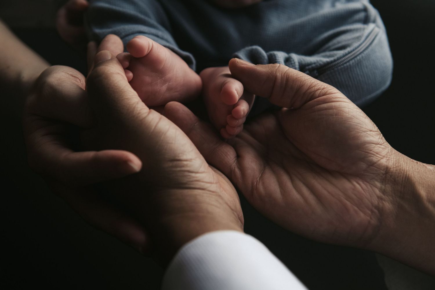 Close-up of gentle hands cradling tiny newborn feet in soft lighting. Ephemera.
