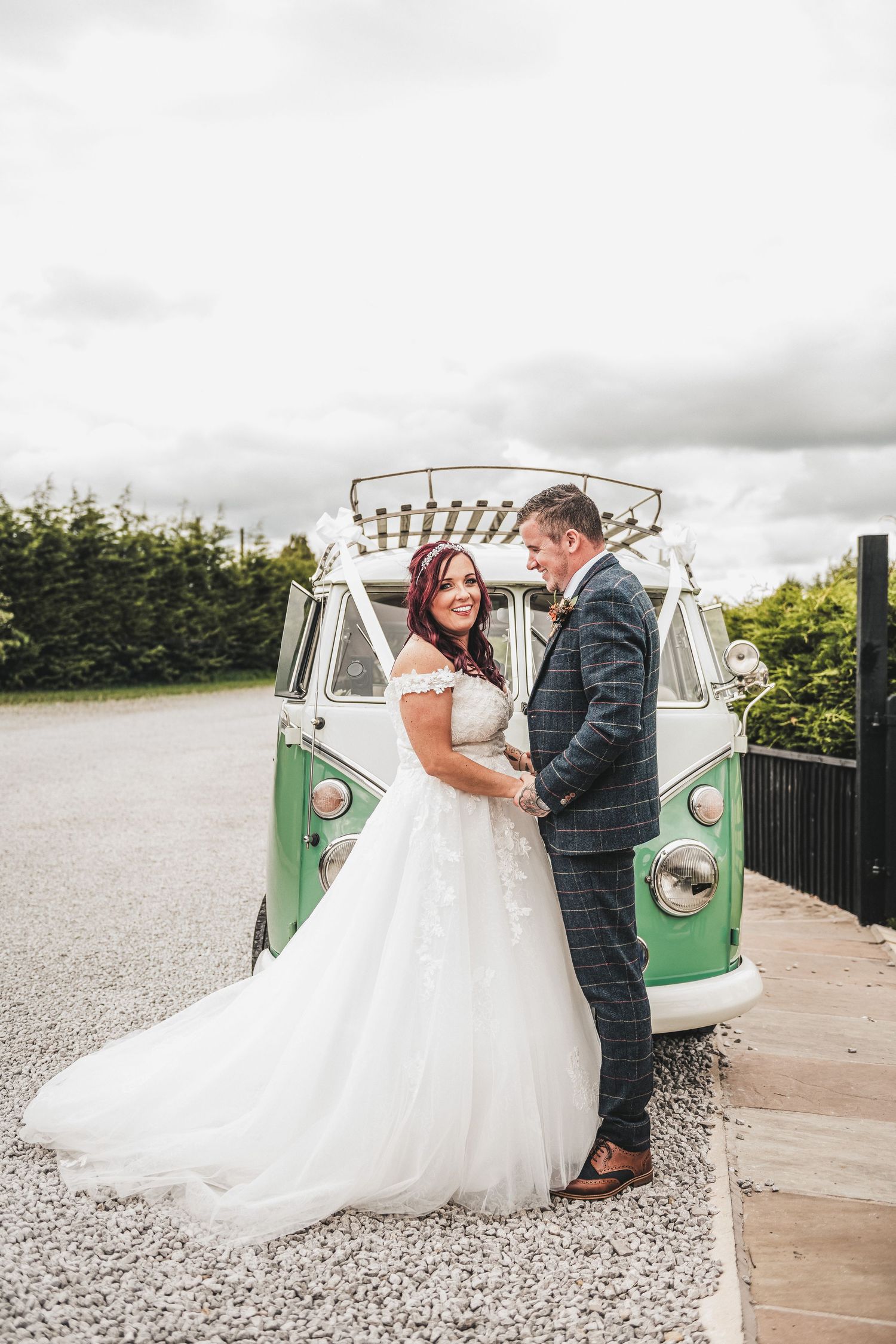 A couple stands in front of a vintage green and white VW bus on their wedding day in a romantic outdoor setting. Ephemera.