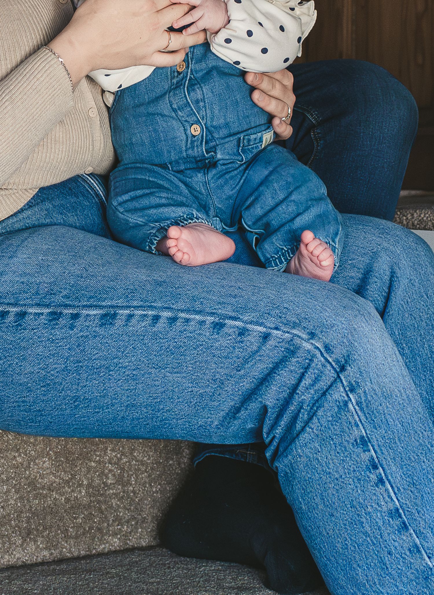Tiny bare feet in denim overalls rest on someone's lap wearing blue jeans. Ephemera.