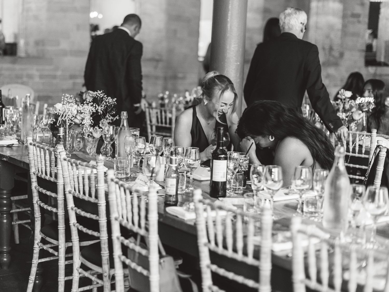 Elegant wedding reception tables set with white linens and floral centerpieces in a formal dining space. Ephemera.