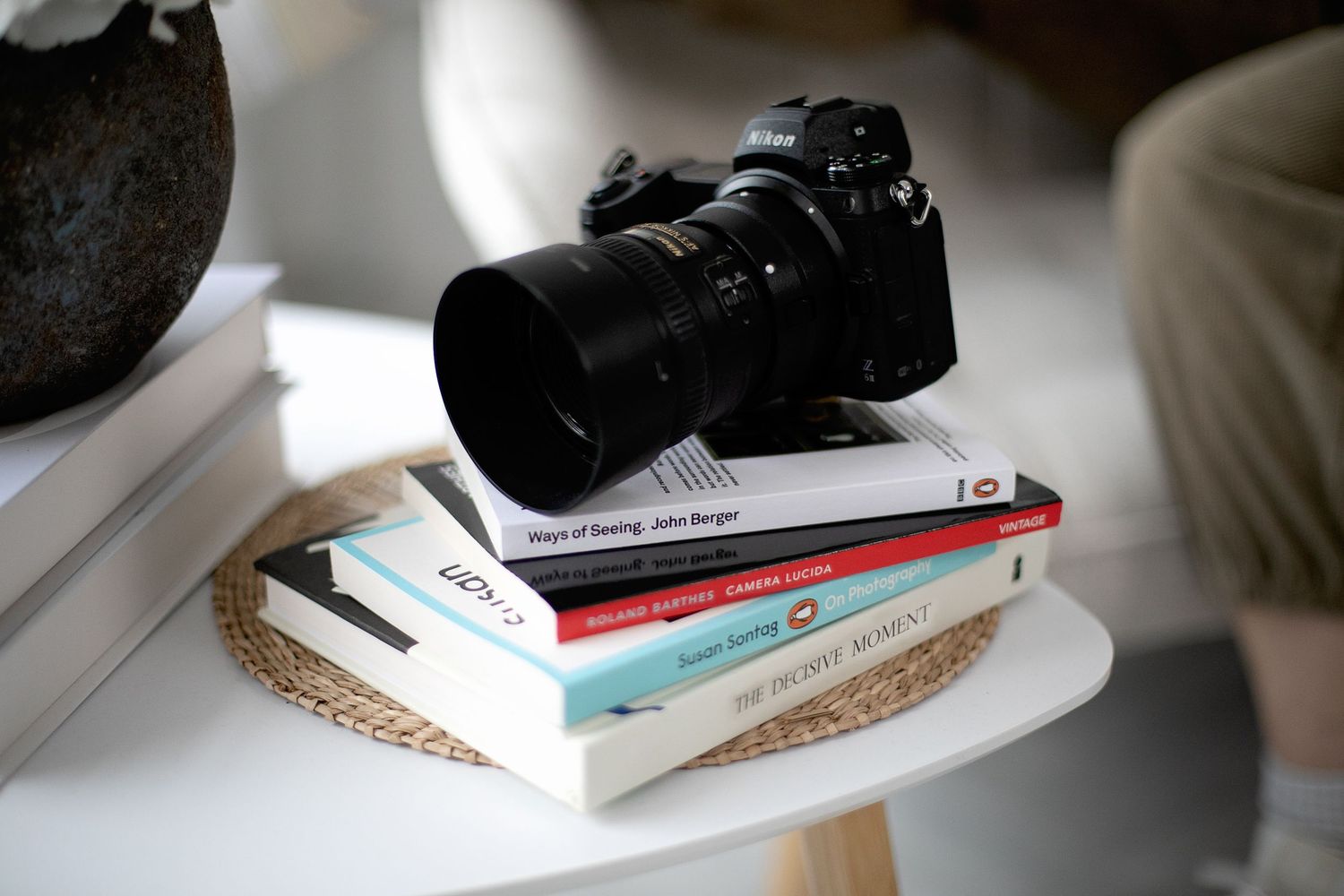 Professional camera and lens resting on stack of books on white side table. Ephemera.