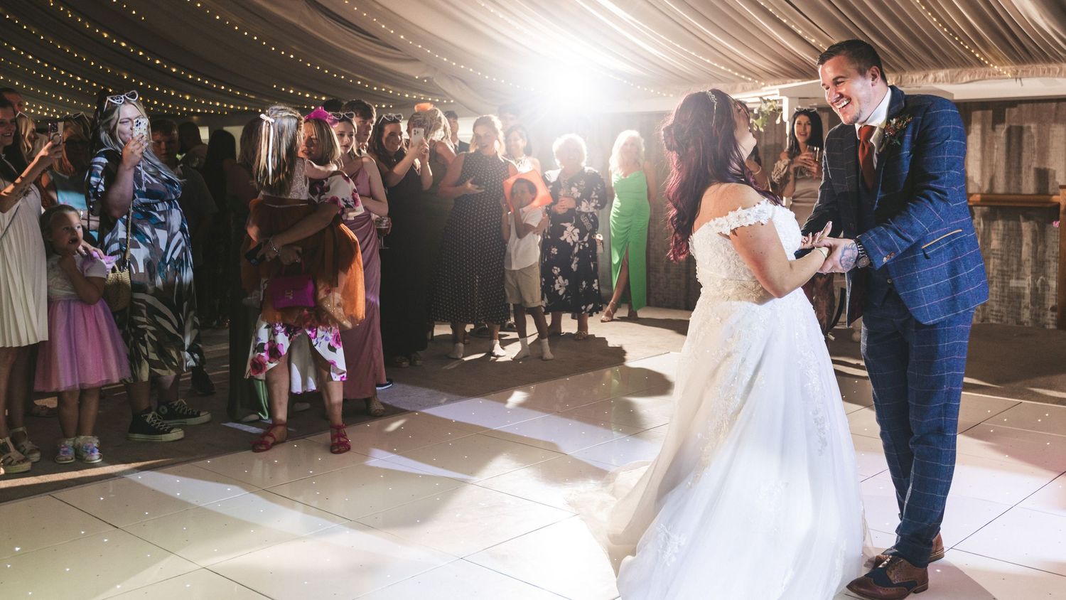 Wedding reception under draped fabric ceiling with string lights and gathered guests. Ephemera.