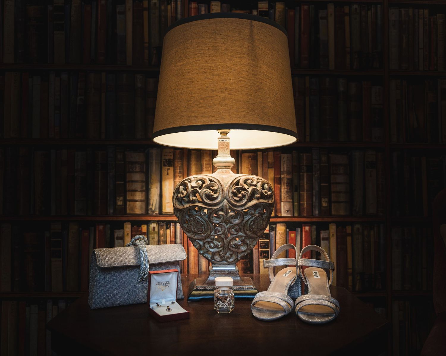 Wedding accessories including bridal shoes and jewelry displayed against dark bookshelves. Ephemera.