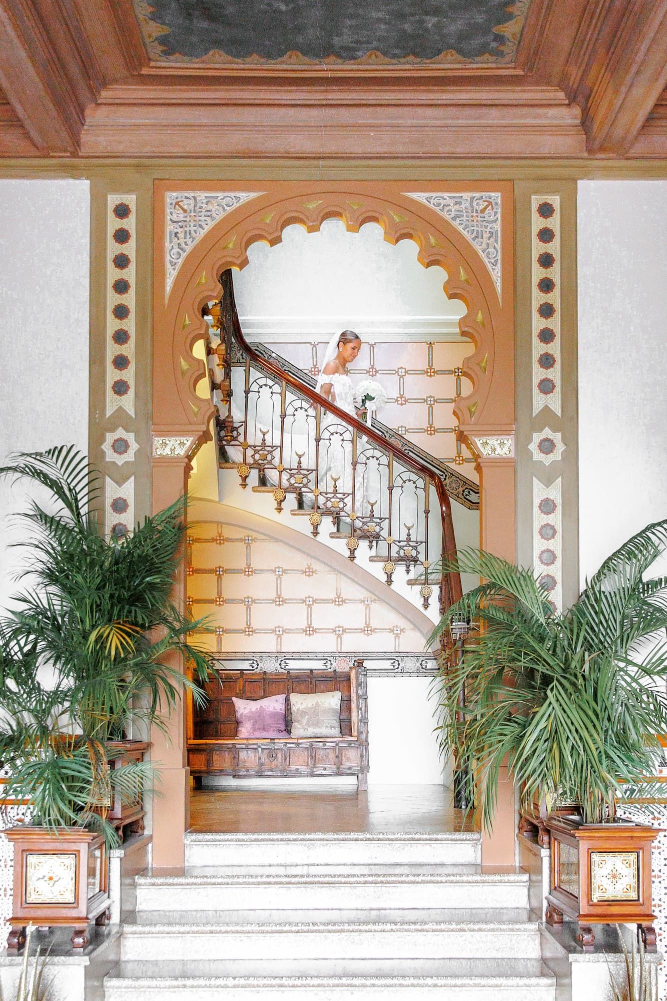 Elegant marble staircase at Gran Villa Rosa with ornate railings and tropical palm plants decorating a grand entrance hall.