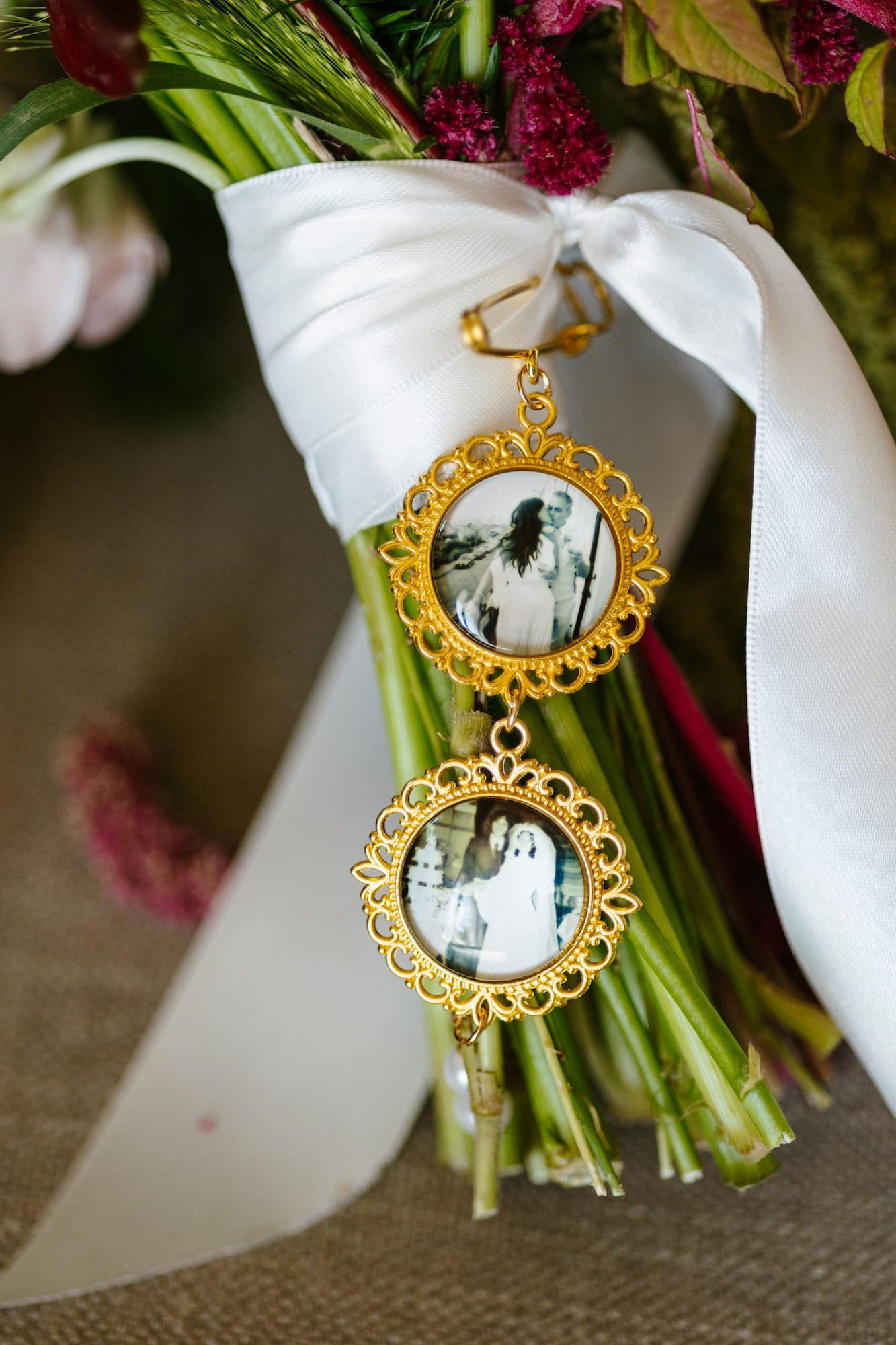 Gold ornate locket charms with black and white photos attached to a bridal bouquet with white ribbon.