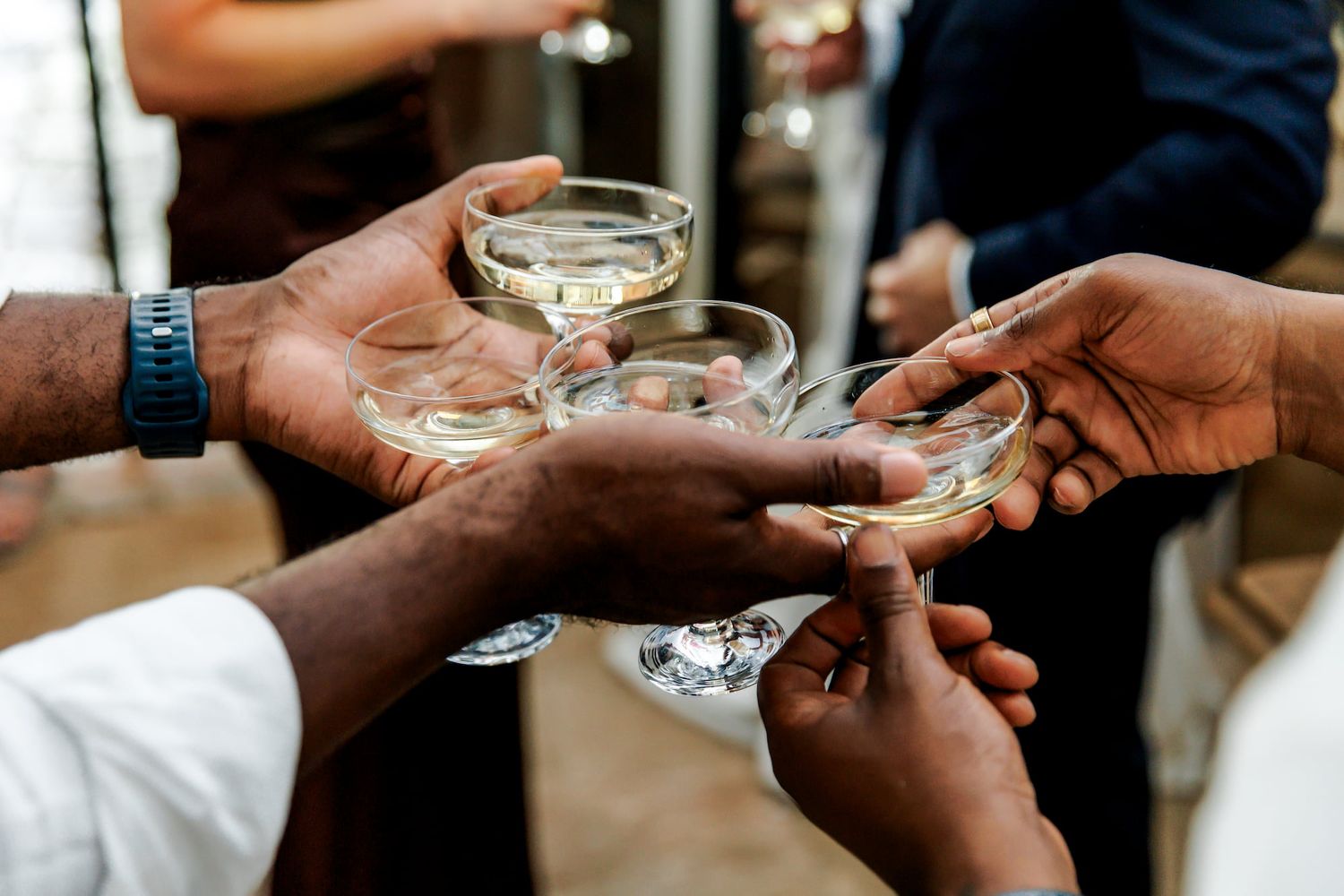 A group of people clinking glasses of white wine together in a celebratory toast at a social gathering.