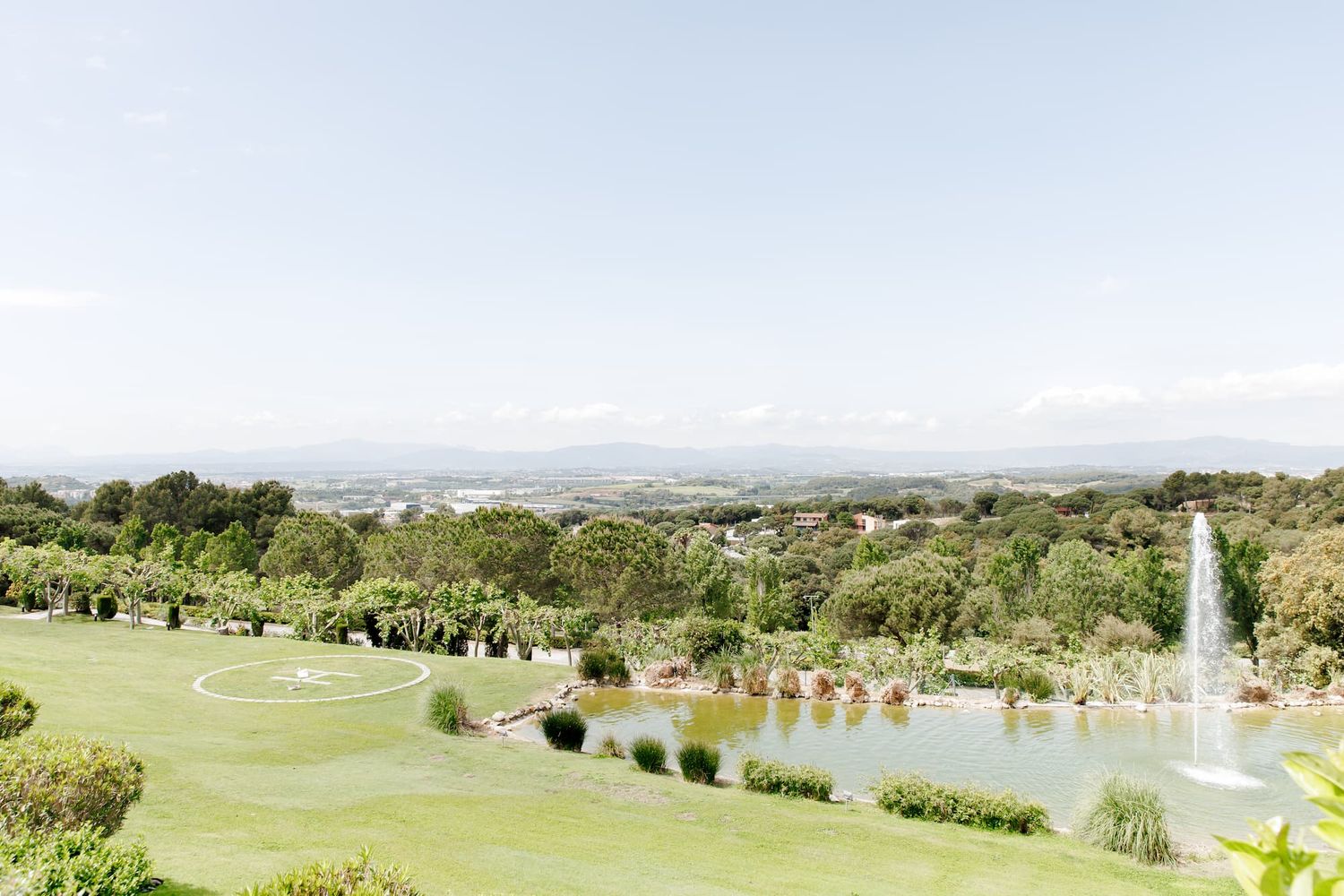 Lush green golf course with a serene pond, fountain, and panoramic views of the city under a clear blue sky.