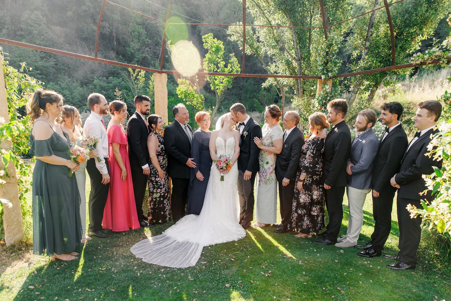 Wedding guests gather in a lush garden setting during an outdoor ceremony on a sunny afternoon.