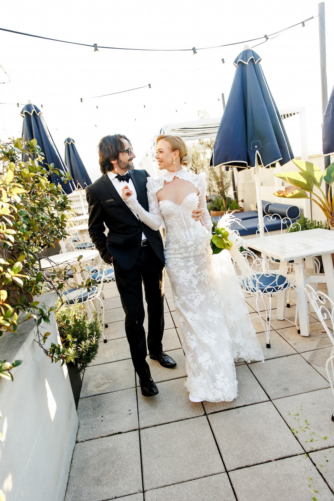 A couple shares a romantic dance together on an outdoor patio with blue umbrellas and greenery in the background.