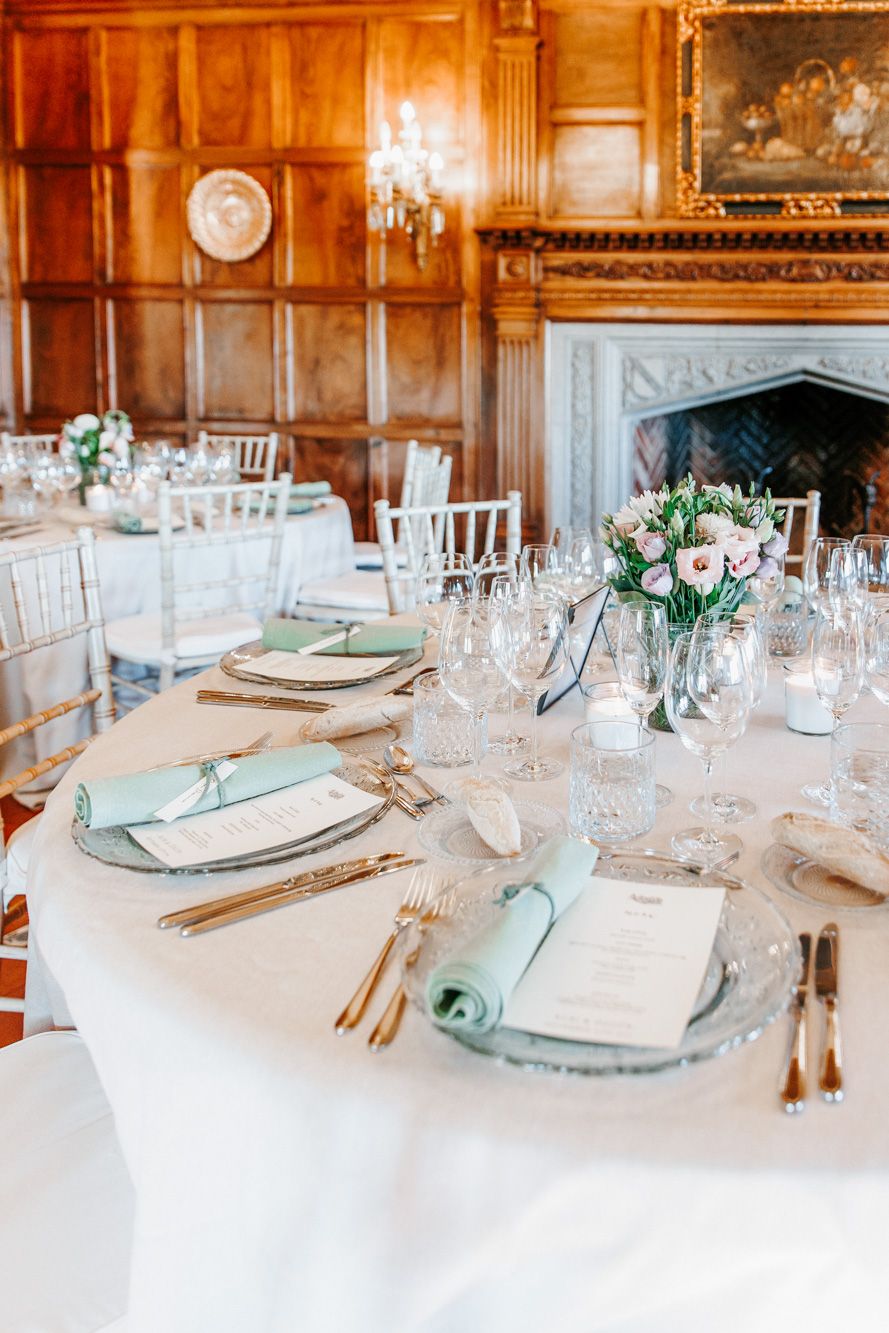 Elegant wedding reception table with mint napkins, gold cutlery, crystal glasses, and floral centerpieces.