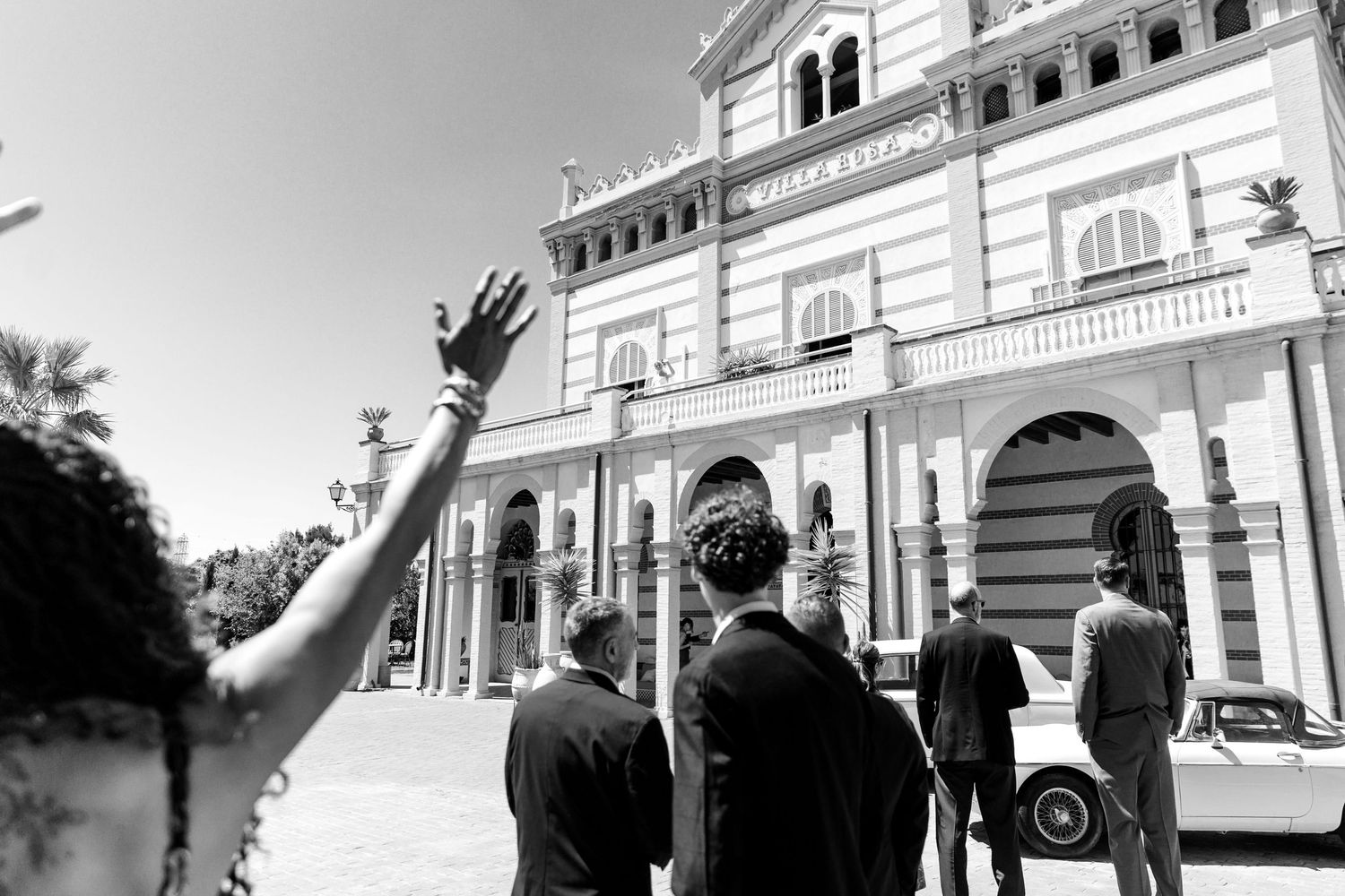 A photo of the bride is greeting her guests from the balcony of the wedding venue