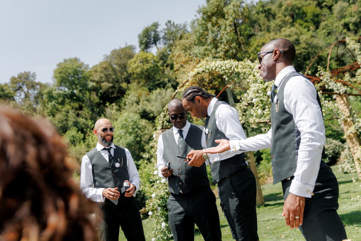 Groomsmen in gray vests and dark suits are laughing outdoors at Mas Huix wedding venue in Barcelona