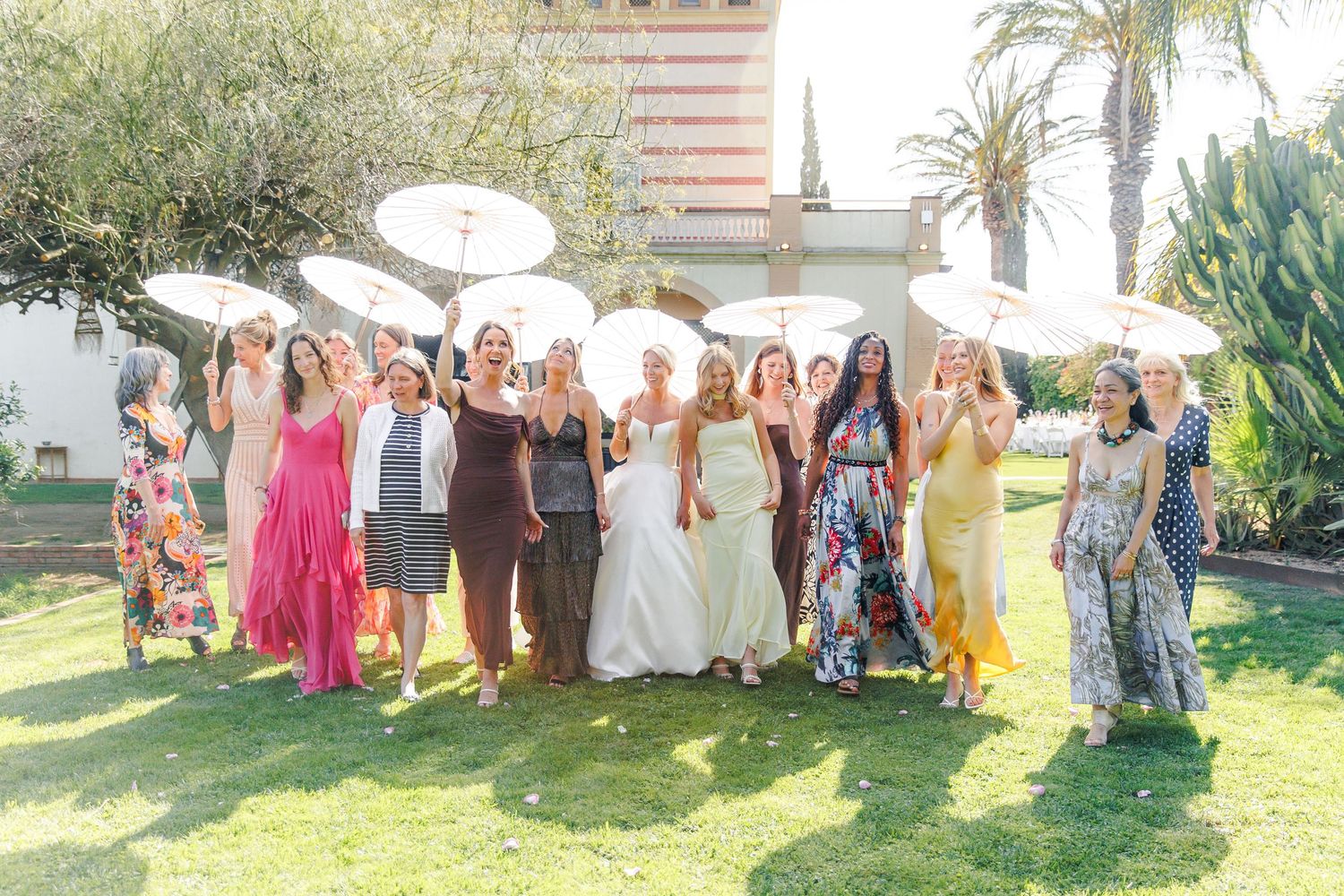 The bride and her bridesmaids, with summer umbrellas, walking in front of the iconic wedding venue in Barcelona