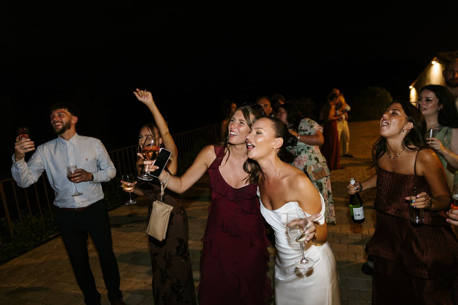 Bride and guests dancing and celebrating joyfully outdoors at a wedding reception at night.
