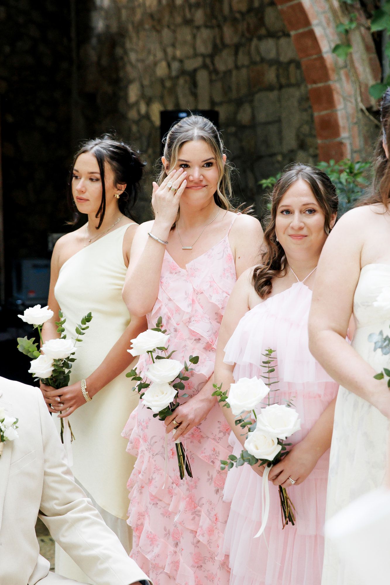 Bridesmaids in white and pink dresses holding white rose bouquets at an outdoor wedding ceremony.