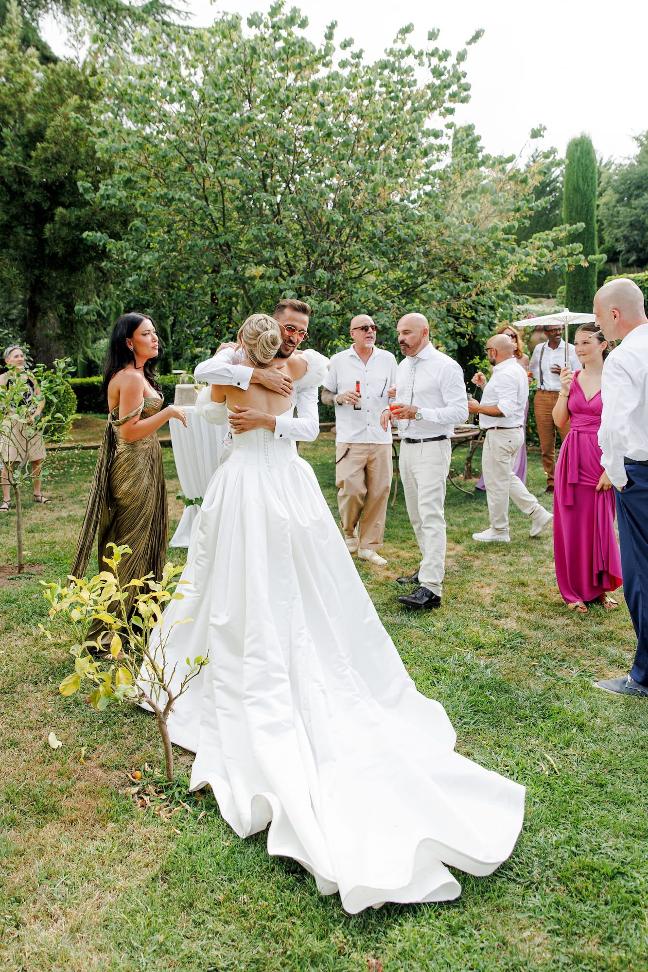 Bride in a white ball gown embracing a guest at an outdoor wedding reception on a sunny day.