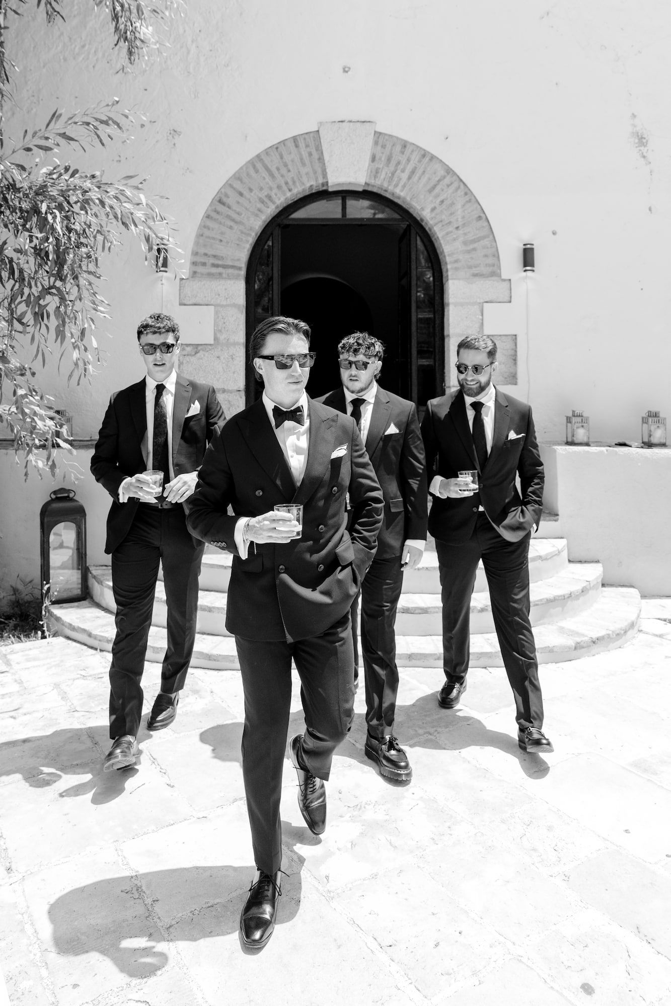 Black and white photo of groom and groomsmen in black suits and sunglasses walking at wedding venue newr Barcelona