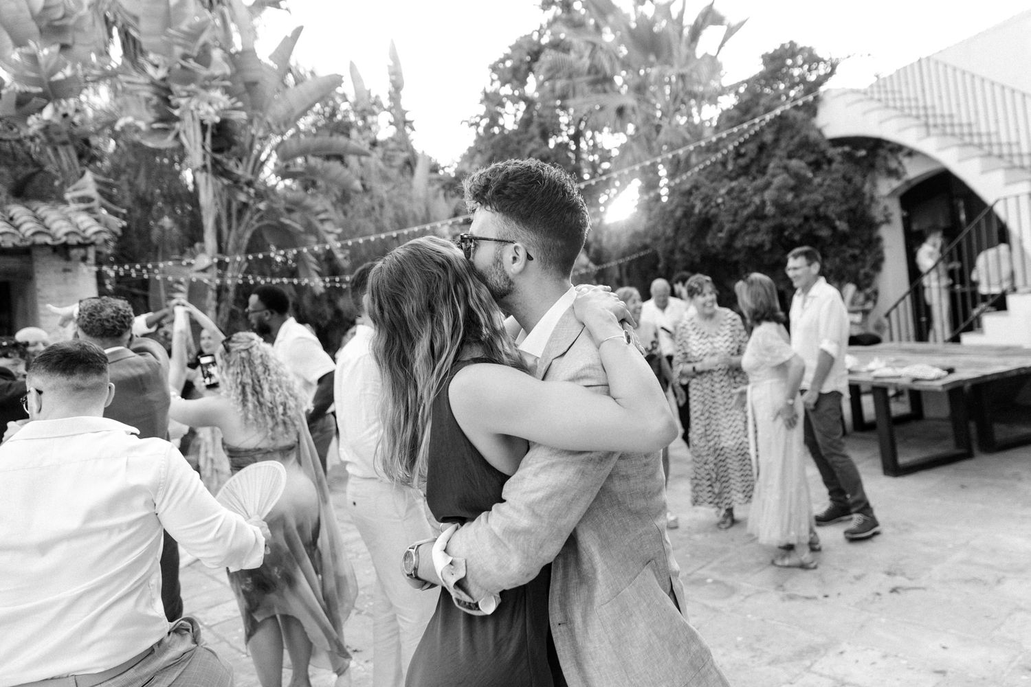 Black and white photo of a couple sharing a kiss while dancing at an outdoor wedding reception.