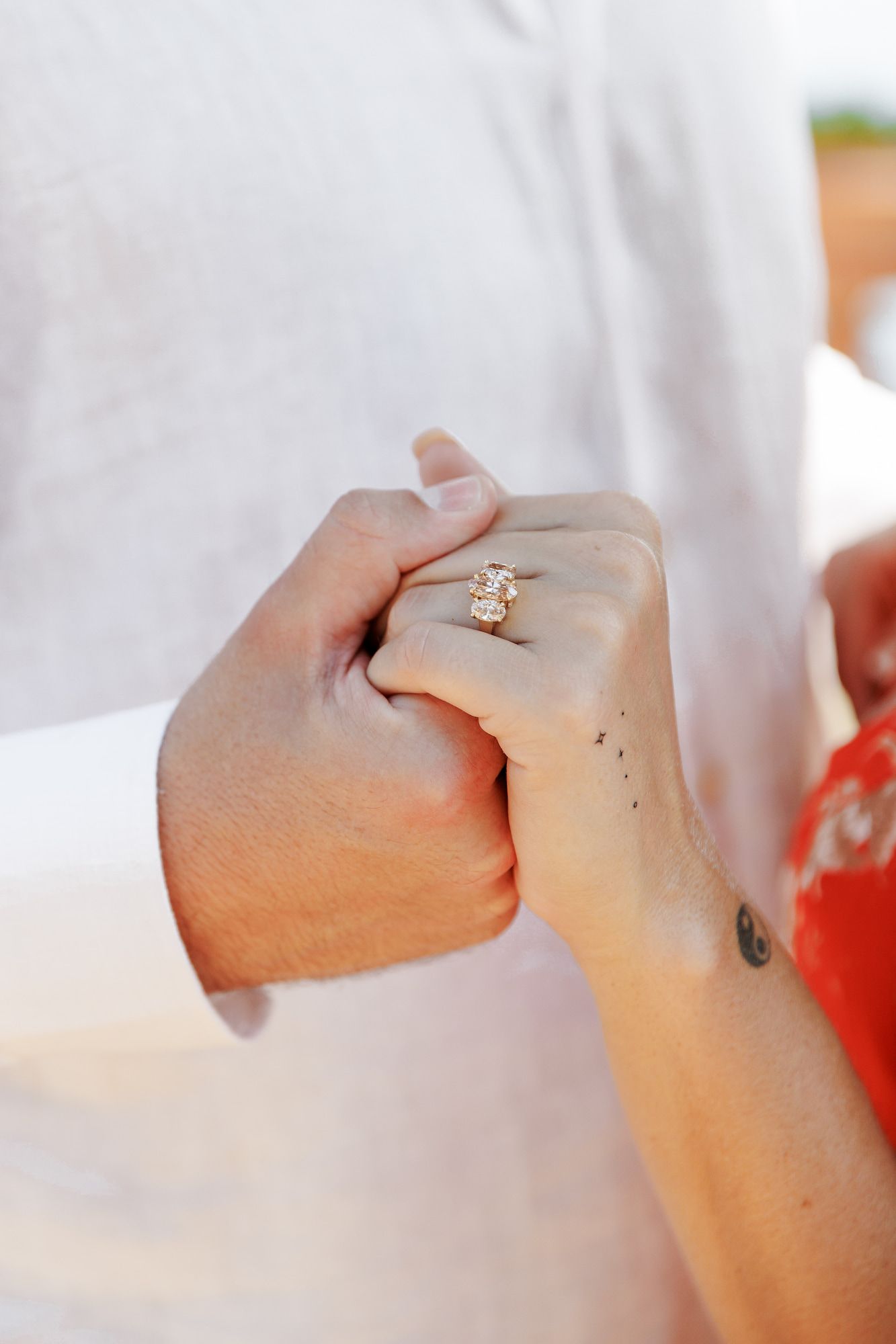 Close-up of a couple holding hands, showcasing a beautiful oval diamond engagement ring on the woman's finger.